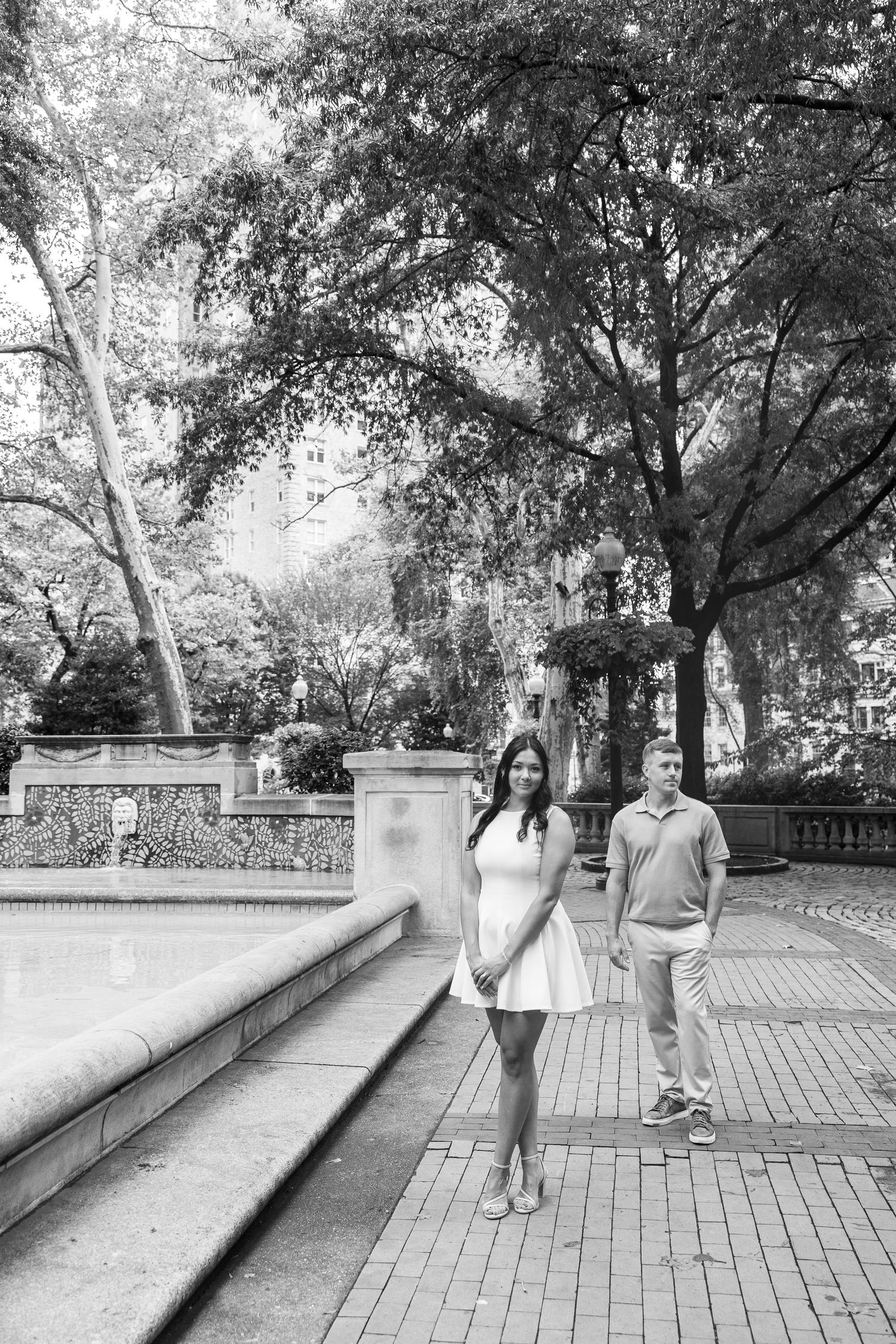 A couple poses playfully on a brick pathway in a park setting.