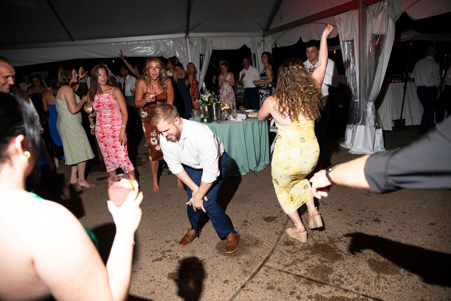 Wedding reception guests dancing on a tent-covered dance floor at night.