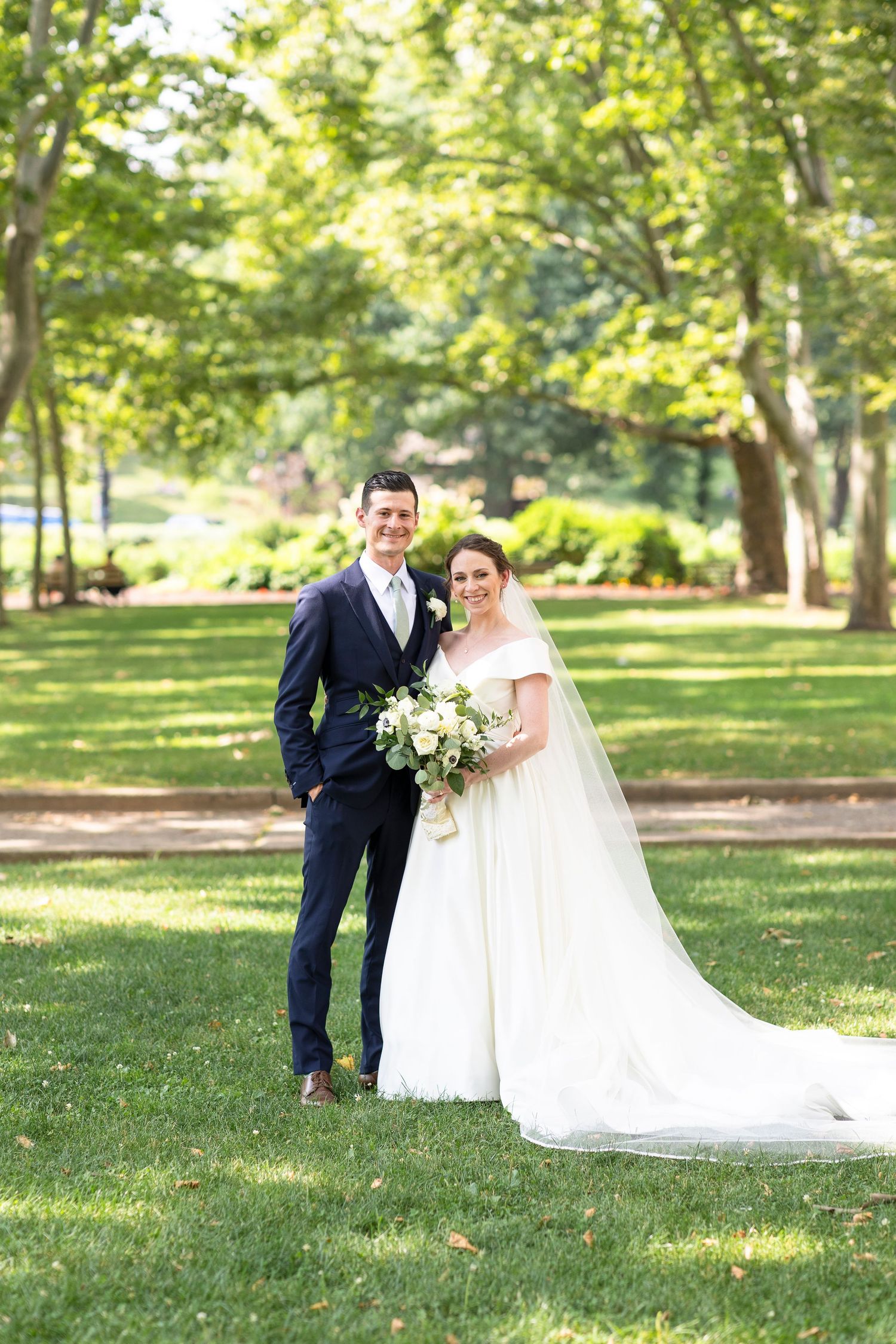 Newlyweds pose for romantic portraits on lush green lawn with white bridal bouquet.