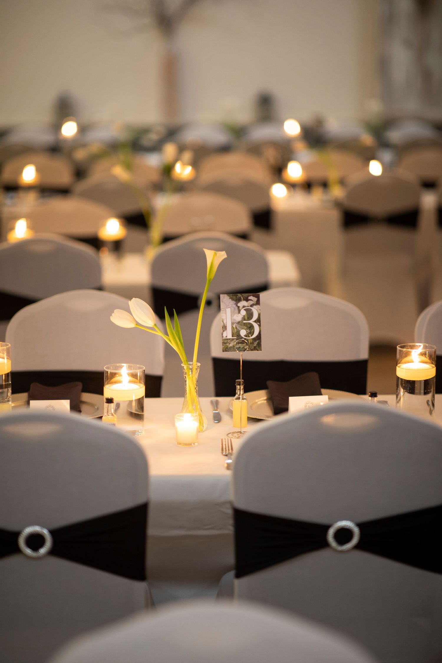 Elegant wedding reception tables with black chairs and glowing candle centerpieces.