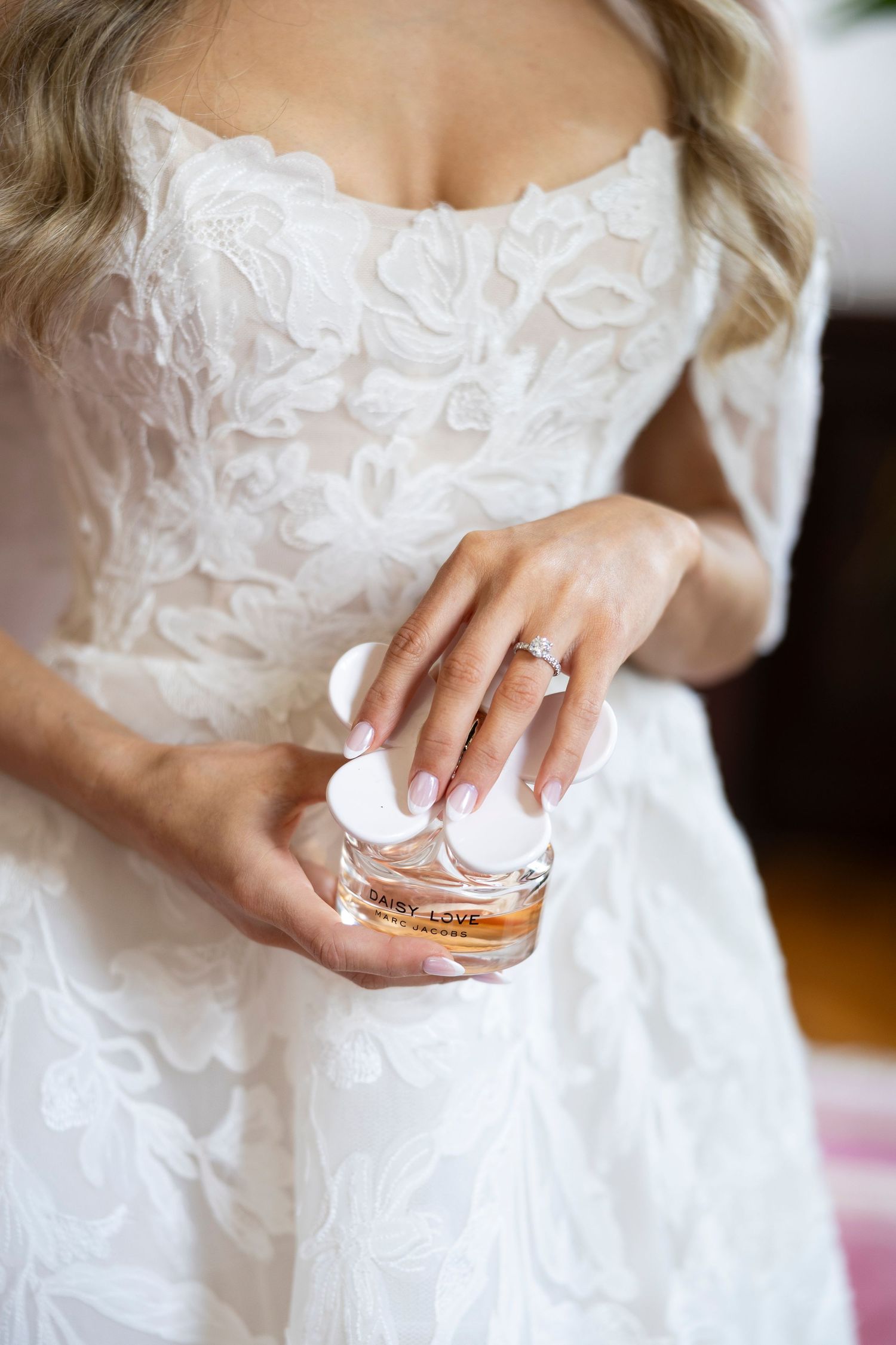 Close-up details of bride's hands holding perfume bottle in lace wedding dress.