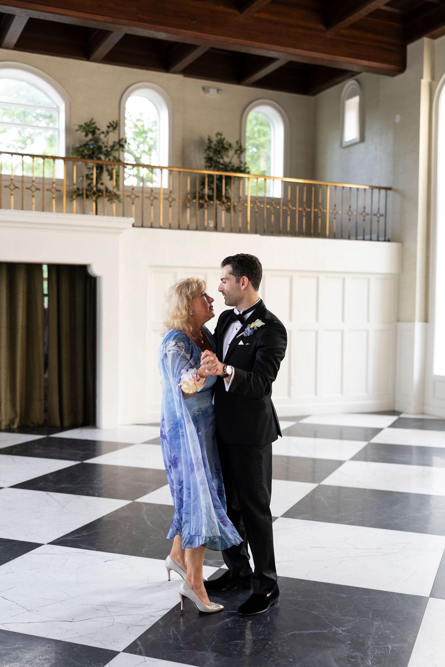 Dancing figures twirl across a grand ballroom with checkerboard floors and wooden beam ceilings.