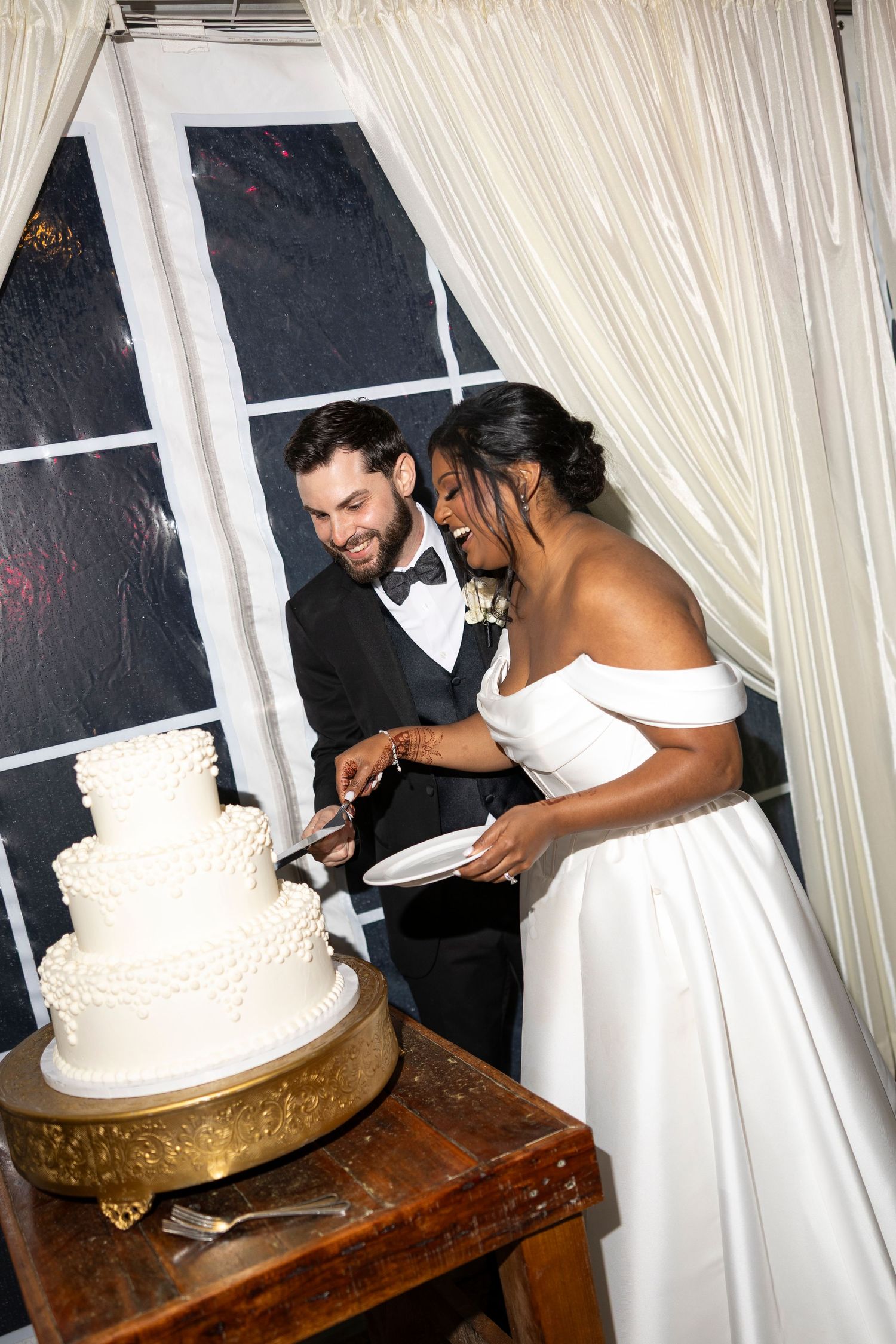 Bride and groom smiling while cutting their white three-tier wedding cake at their reception.