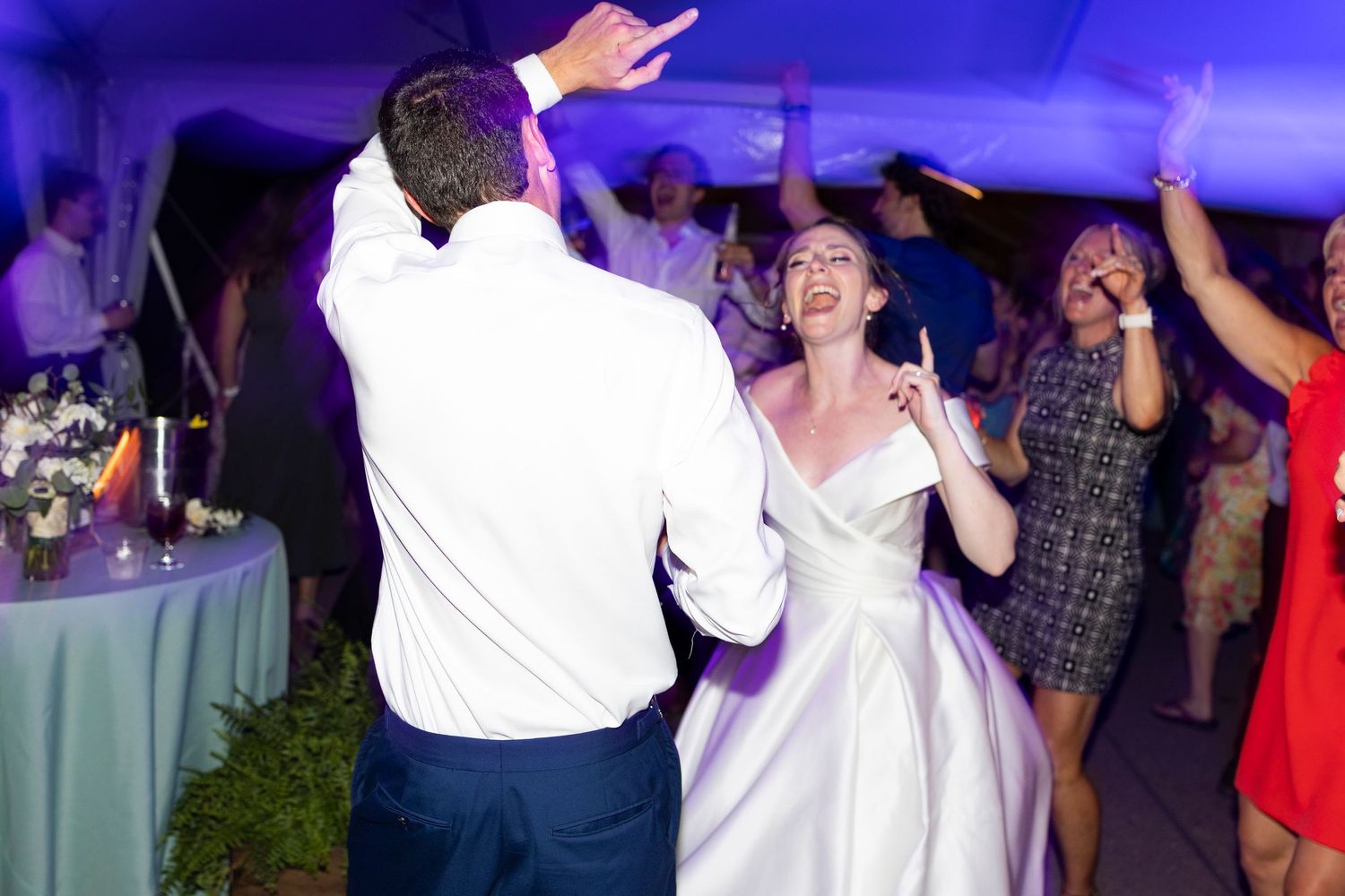 Wedding reception guests dancing and celebrating on a dance floor under blue lighting.