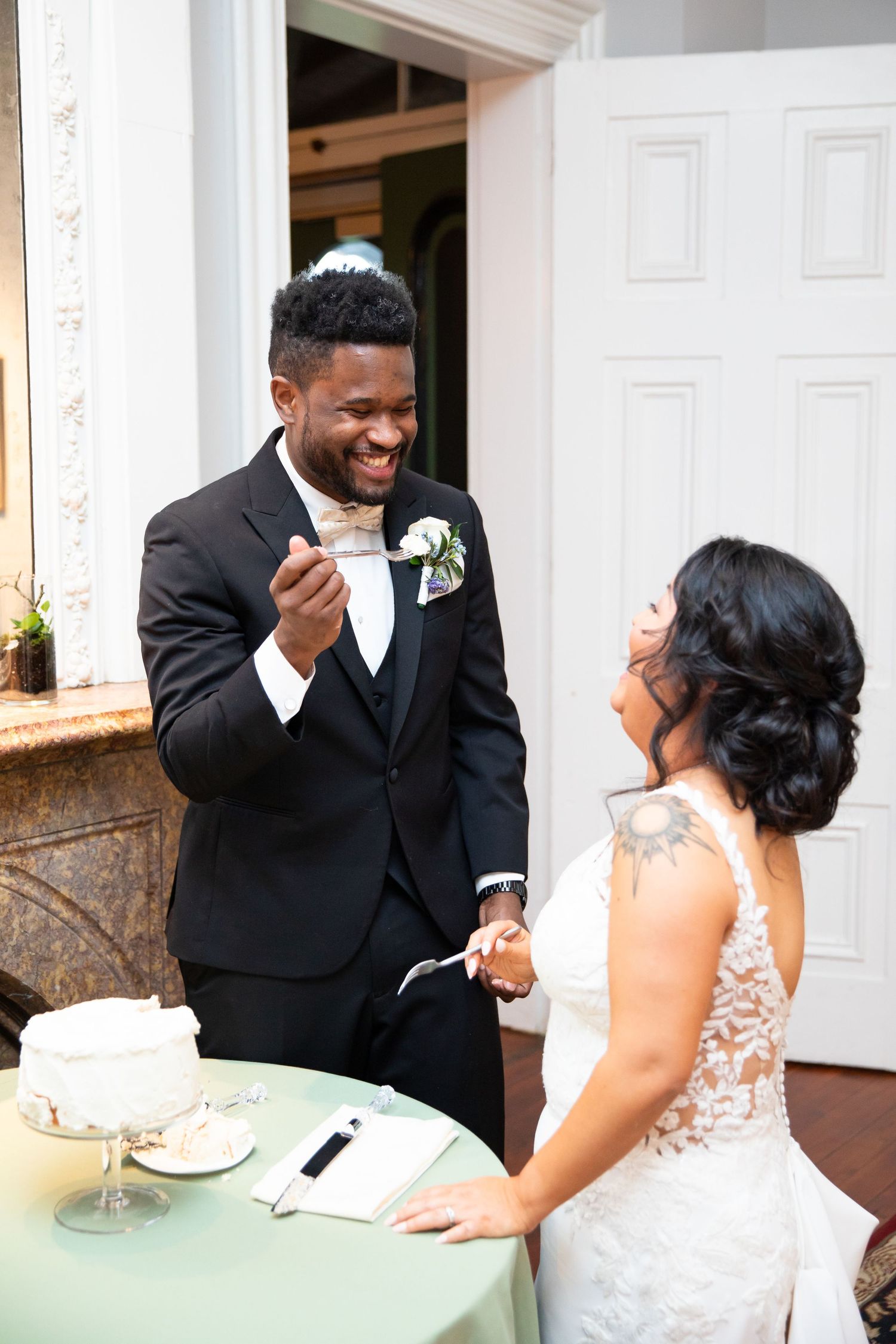 Joyful wedding couple shares laughs while eating cake at their reception.