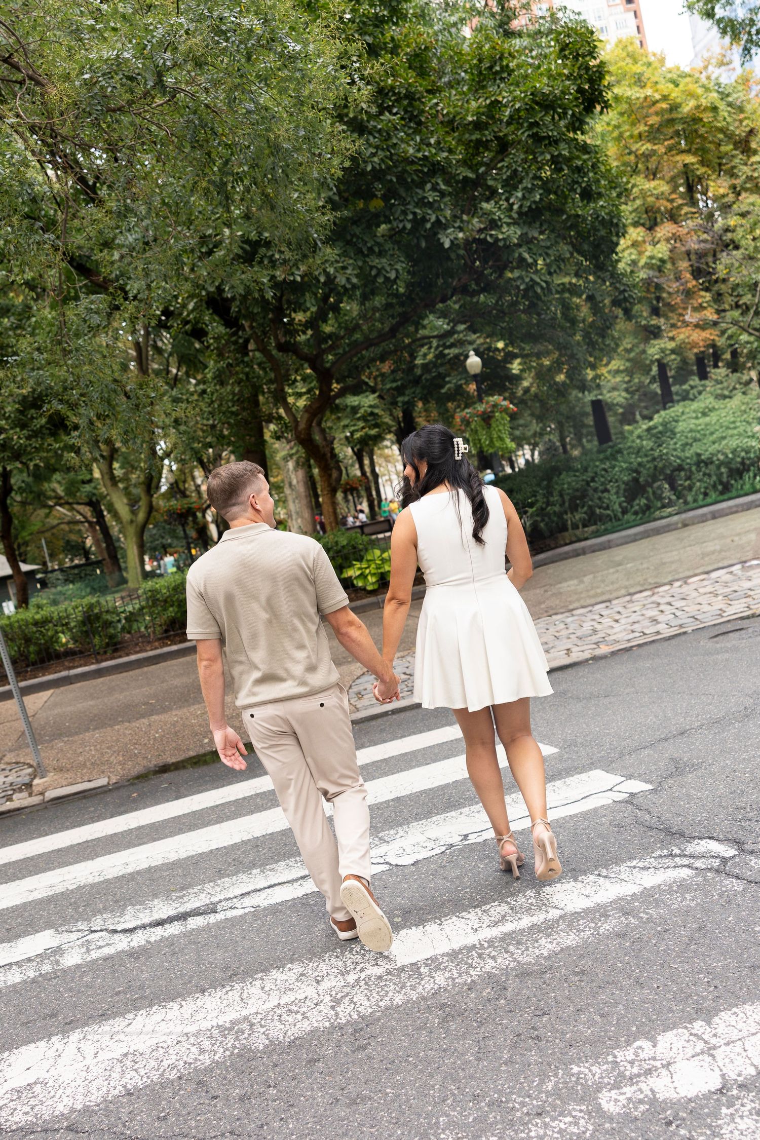 A couple walks across a white crosswalk in a park setting during a romantic photoshoot.
