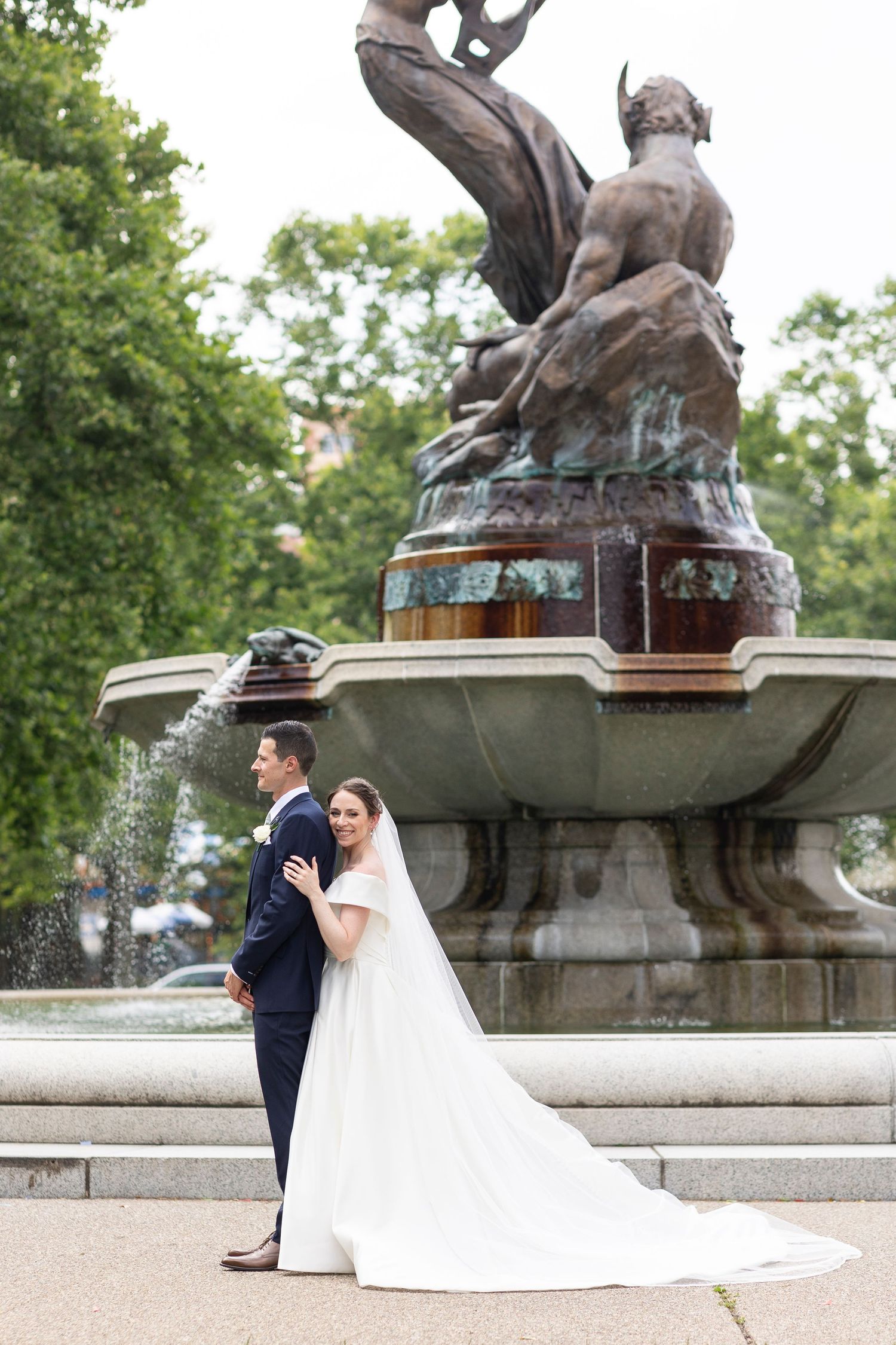 Elegant wedding photos captured by decorative fountain with bronze sculptures in a park setting.