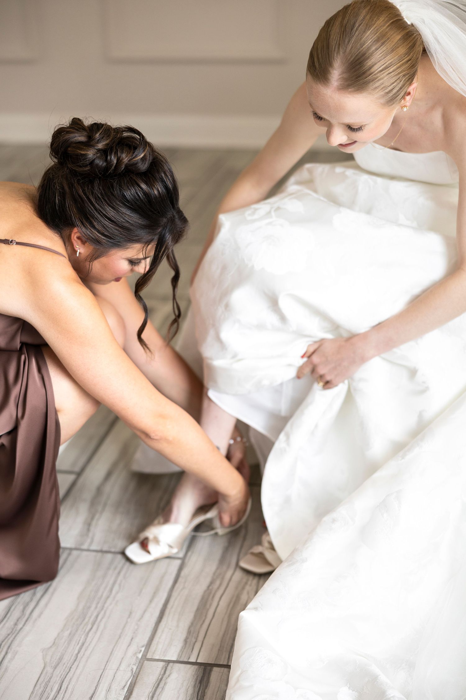 Helper adjusting wedding dress and shoes during bridal preparation.