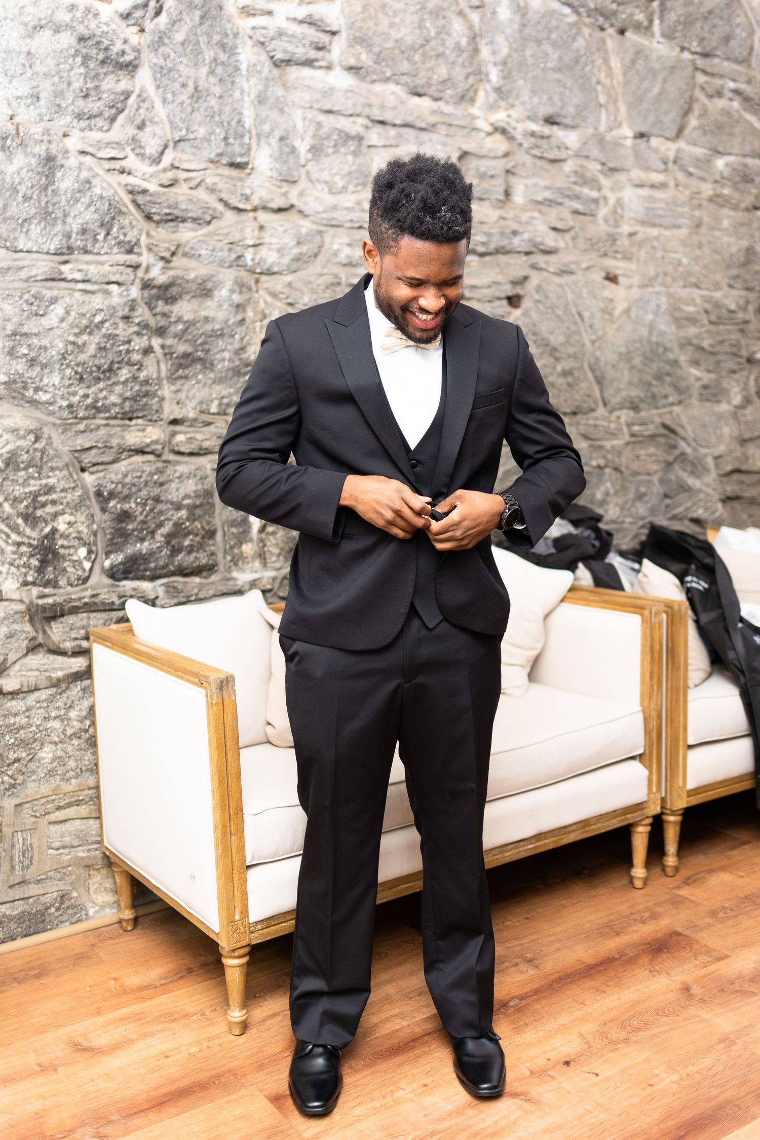 A person in formal attire sits on an elegant white bench against a stone wall.