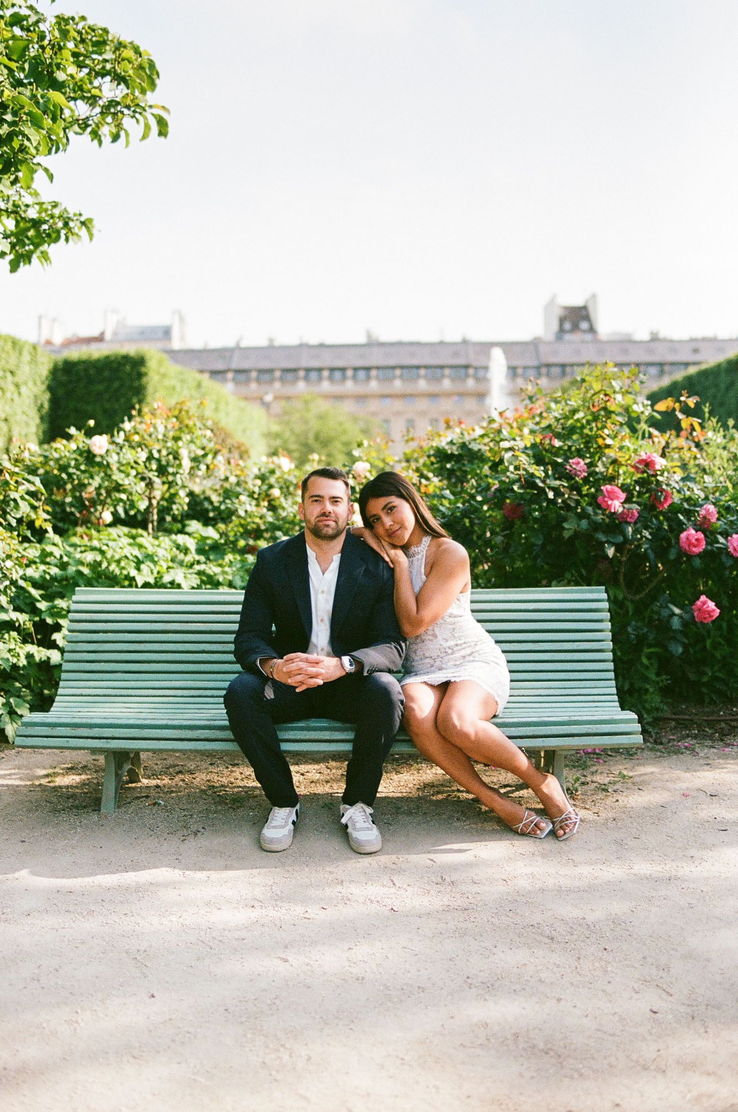 Green park bench surrounded by blooming rose gardens and classical architecture.