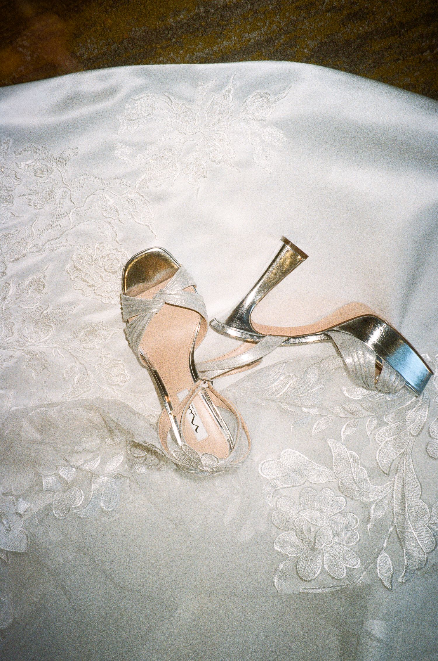 Silver wedding shoes rest elegantly on white lace fabric.