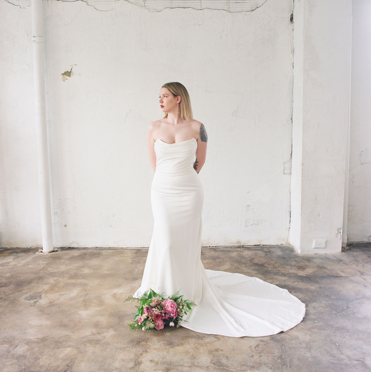 Elegant bridal portrait in a minimalist white industrial space with trailing bouquet.
