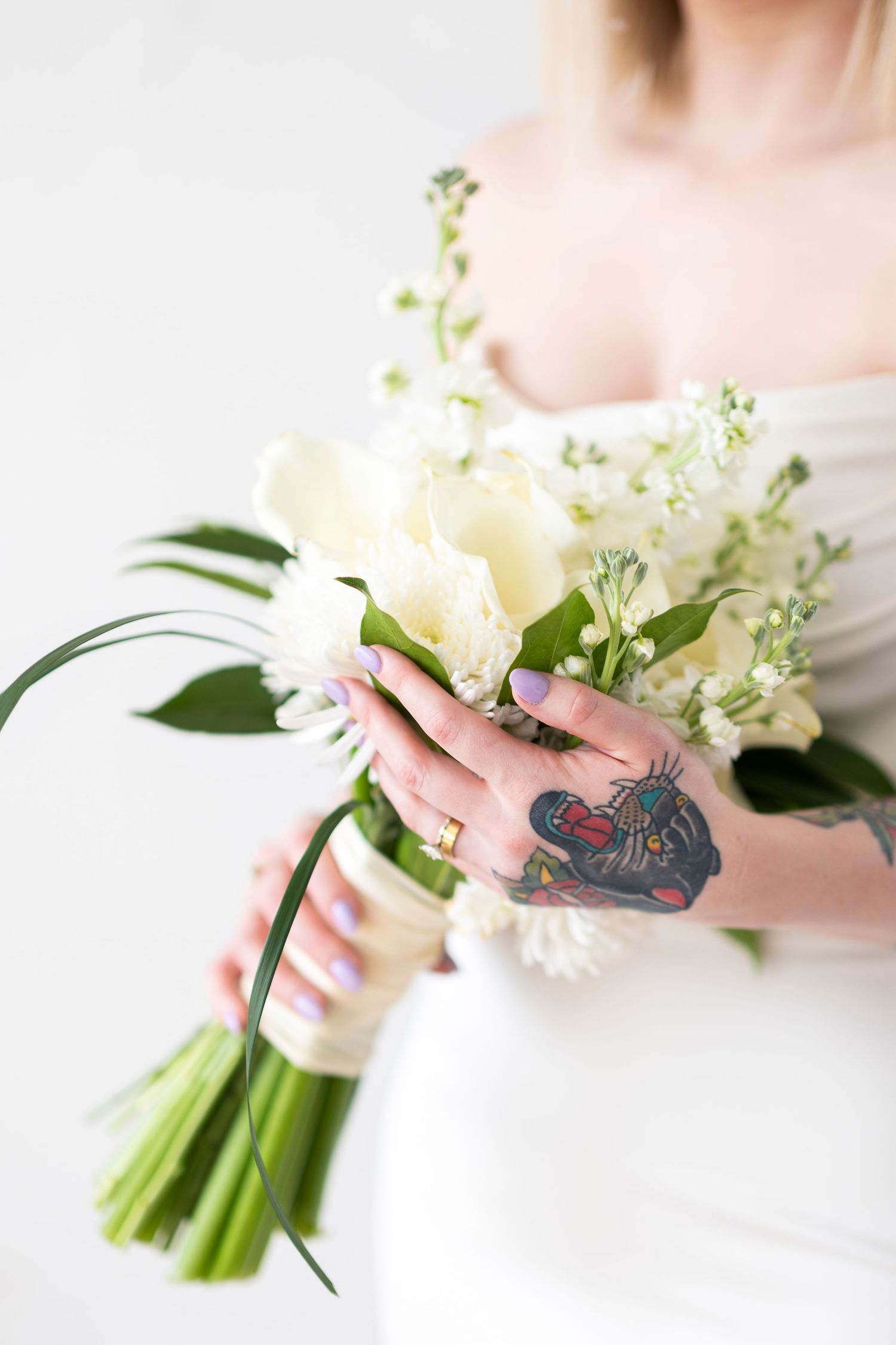 Close-up of hands holding white floral bouquet with visible tattoo art.