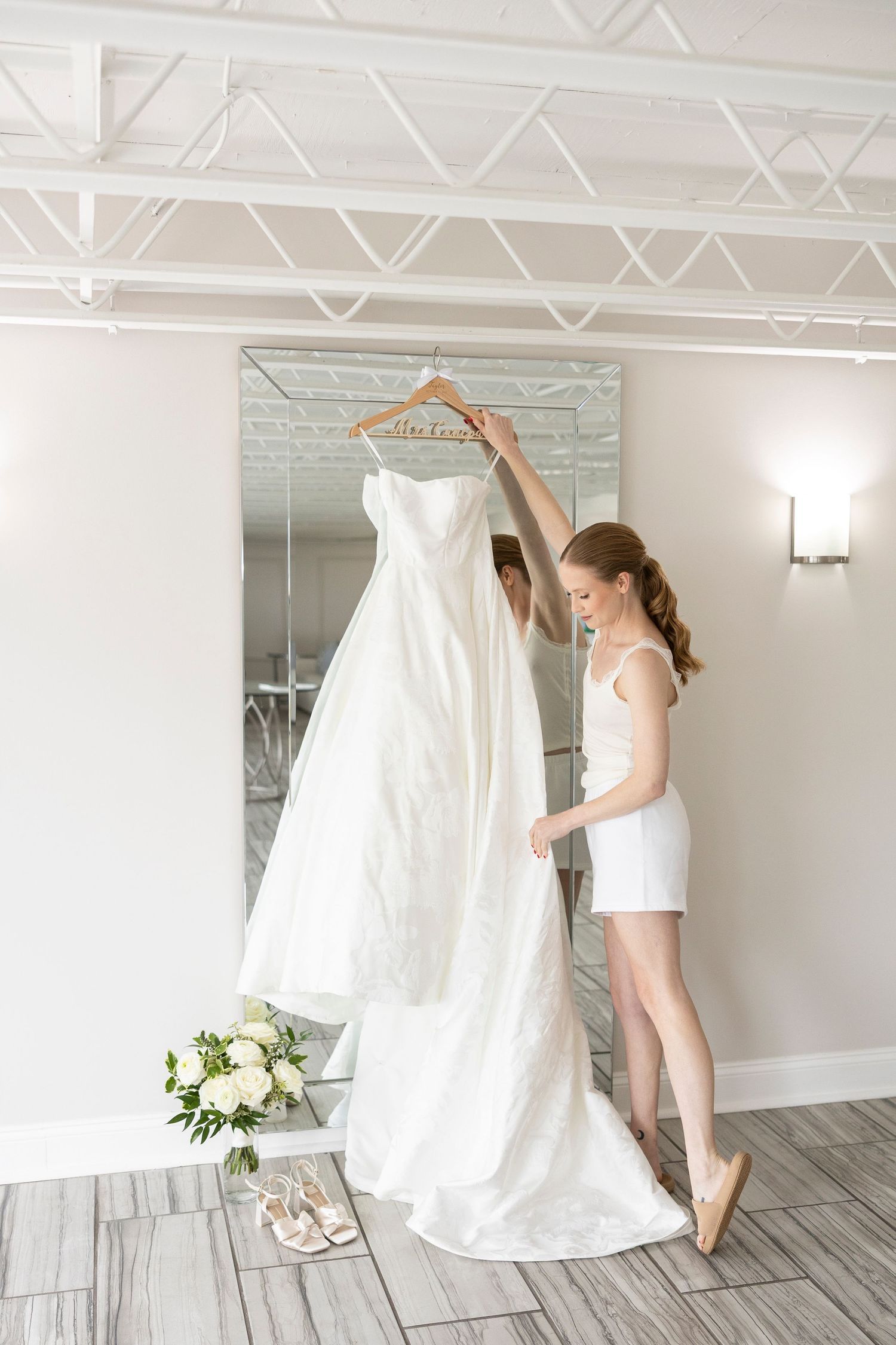 A wedding dress displayed in a bright studio as someone reaches up to adjust it.
