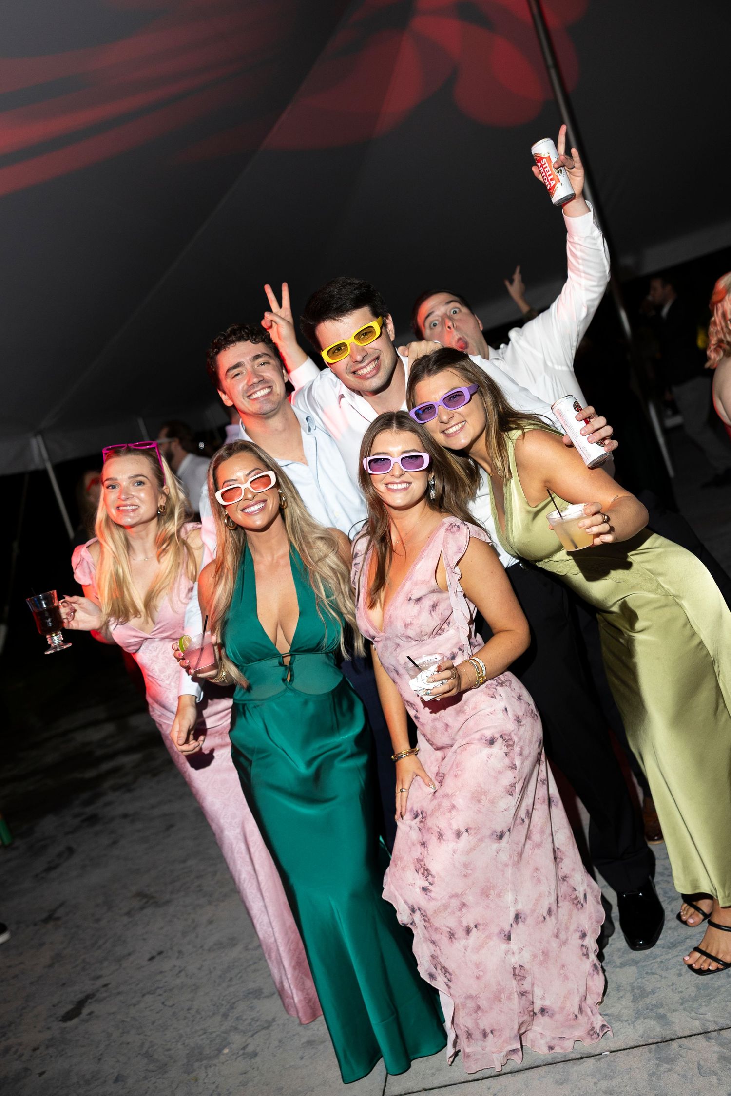 Wedding guests in colorful attire posing with fun party accessories on dance floor.
