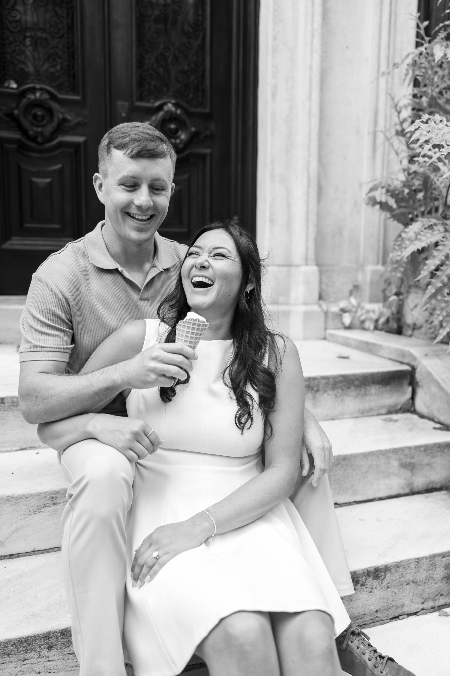 A couple shares ice cream and laughter while sitting on white stone steps.