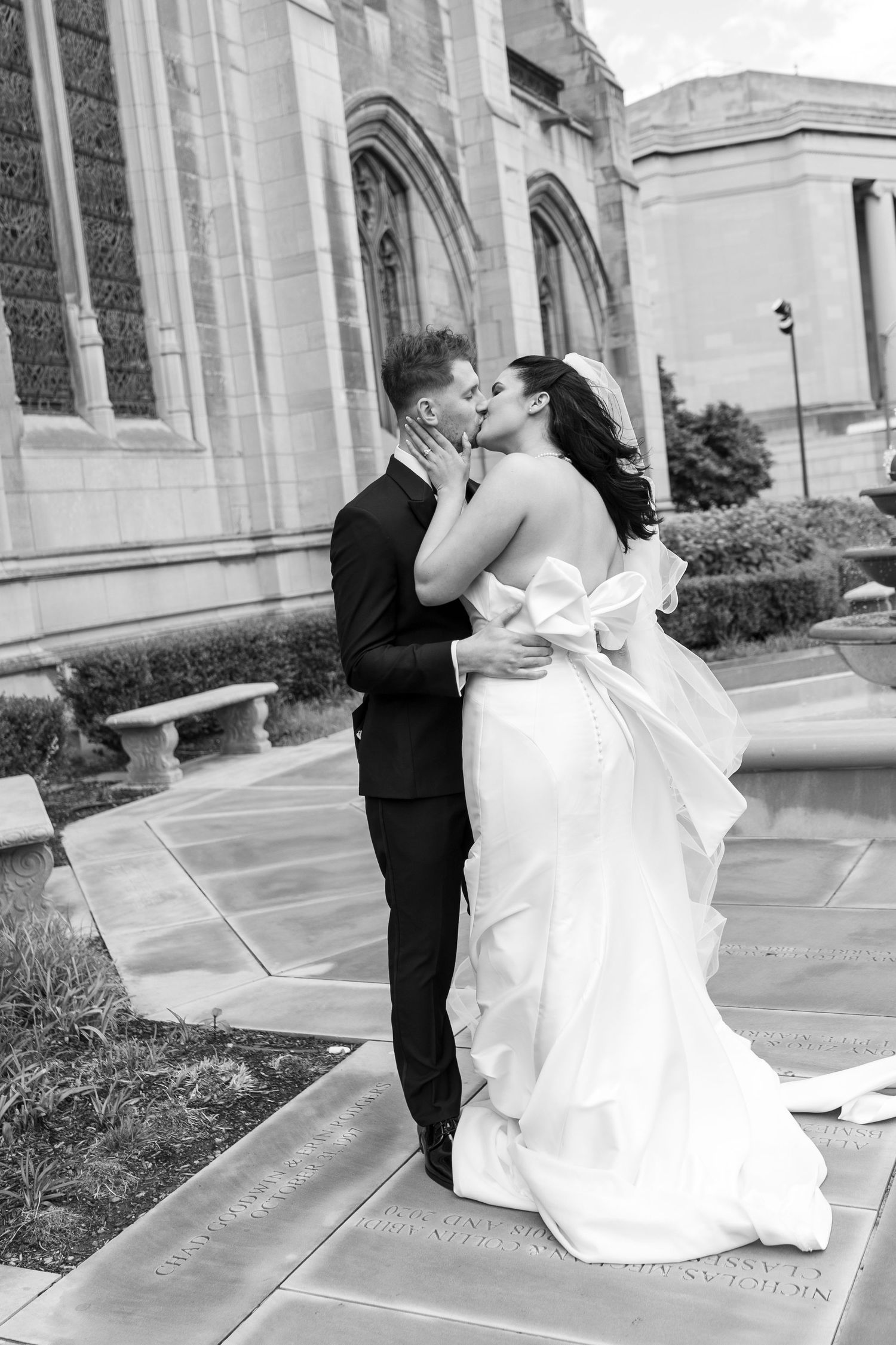 Romantic wedding moment captured in black and white outside ornate stone building with arched architecture.