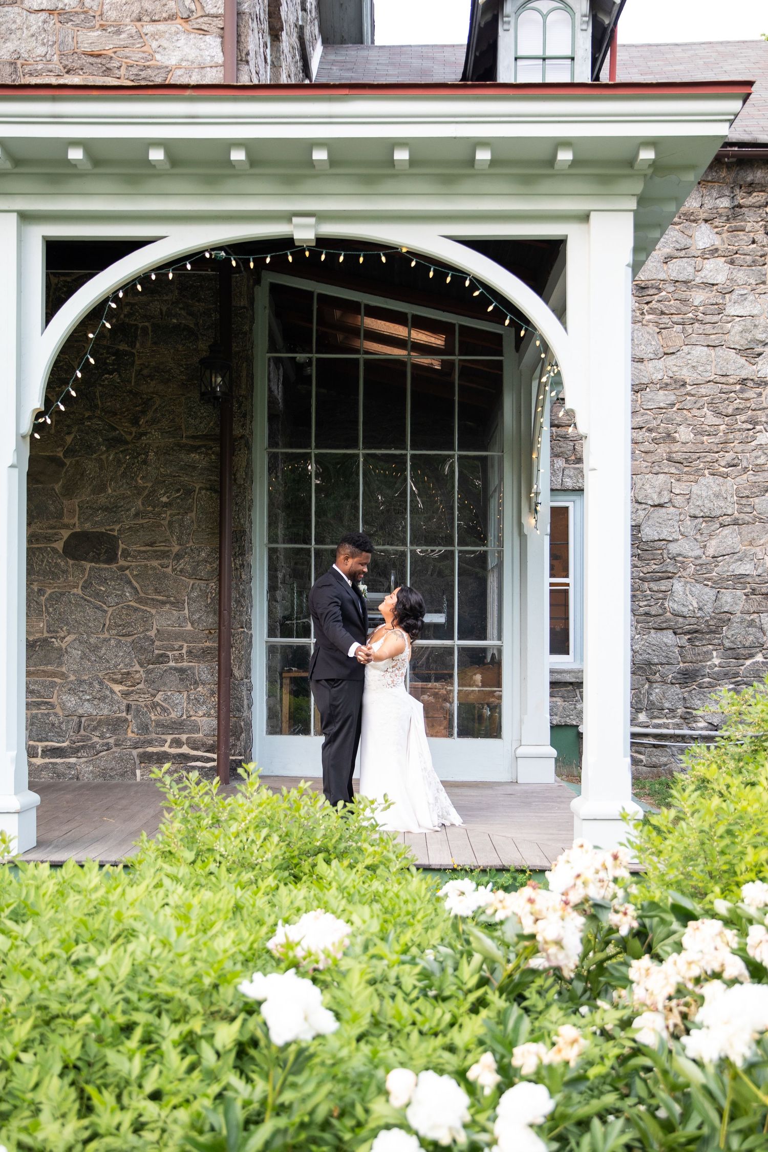 Elegant wedding photos captured on a historic building's porch surrounded by lush greenery.