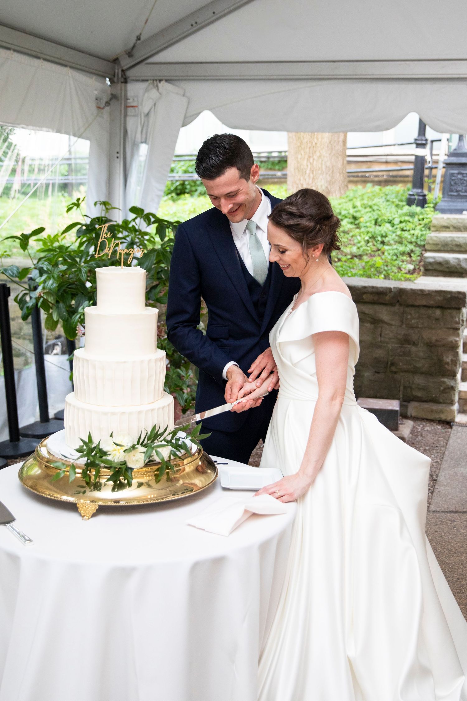 A couple enjoys their wedding cake cutting moment under a white tent reception.