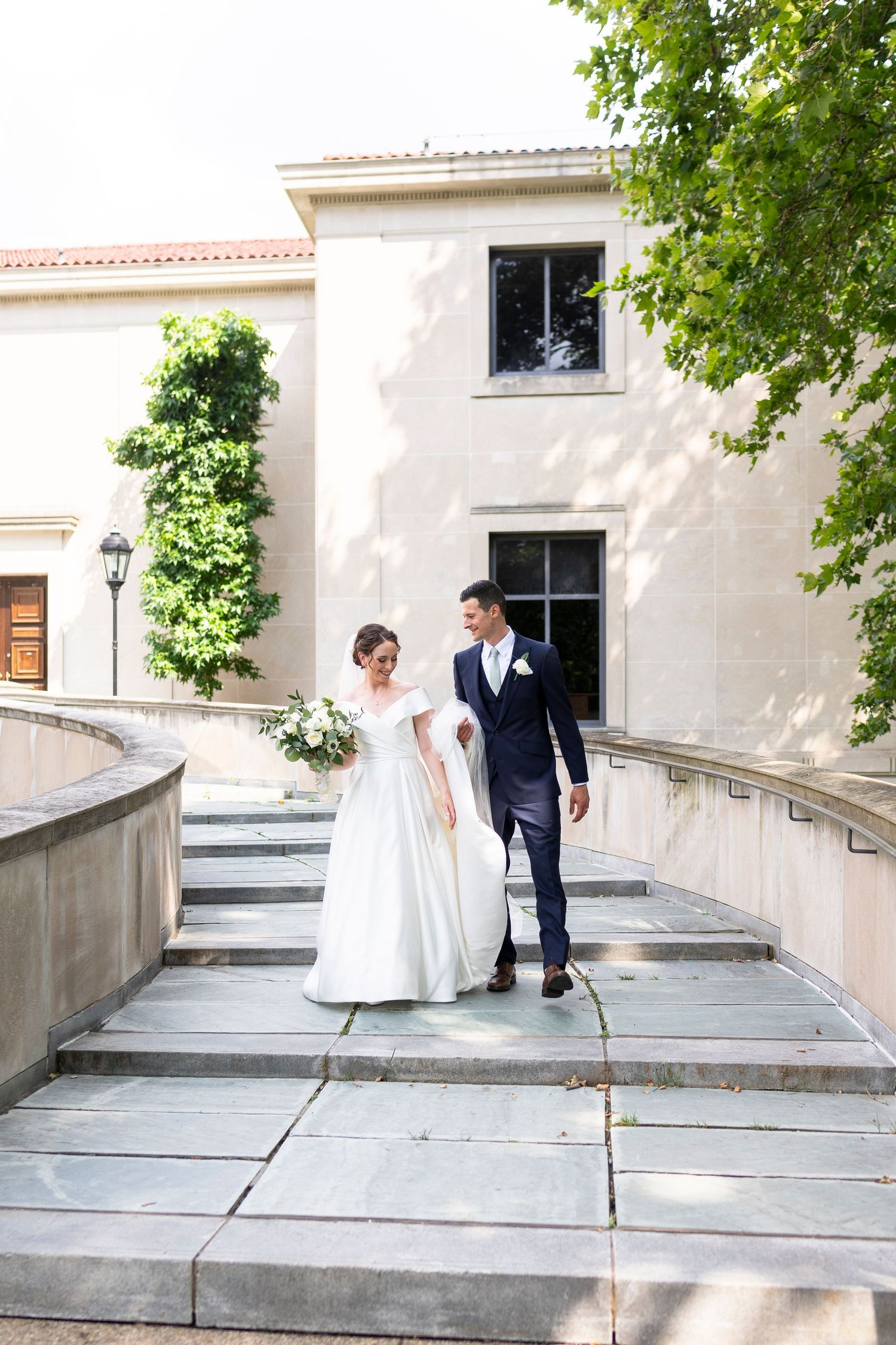 Wedding couple poses on elegant stone steps with white columns and architectural details in the background.