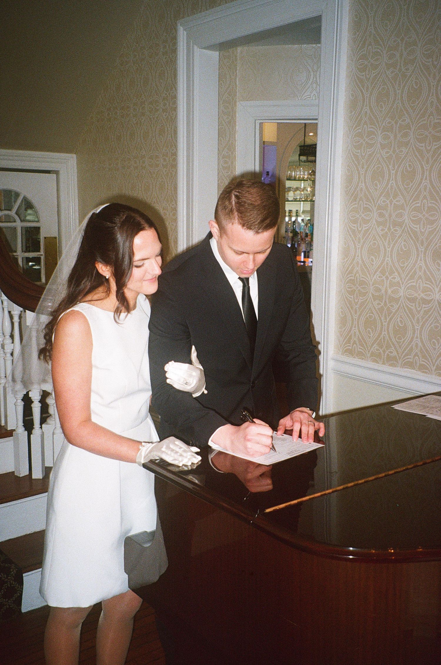 A couple in wedding attire signs documents at a piano.