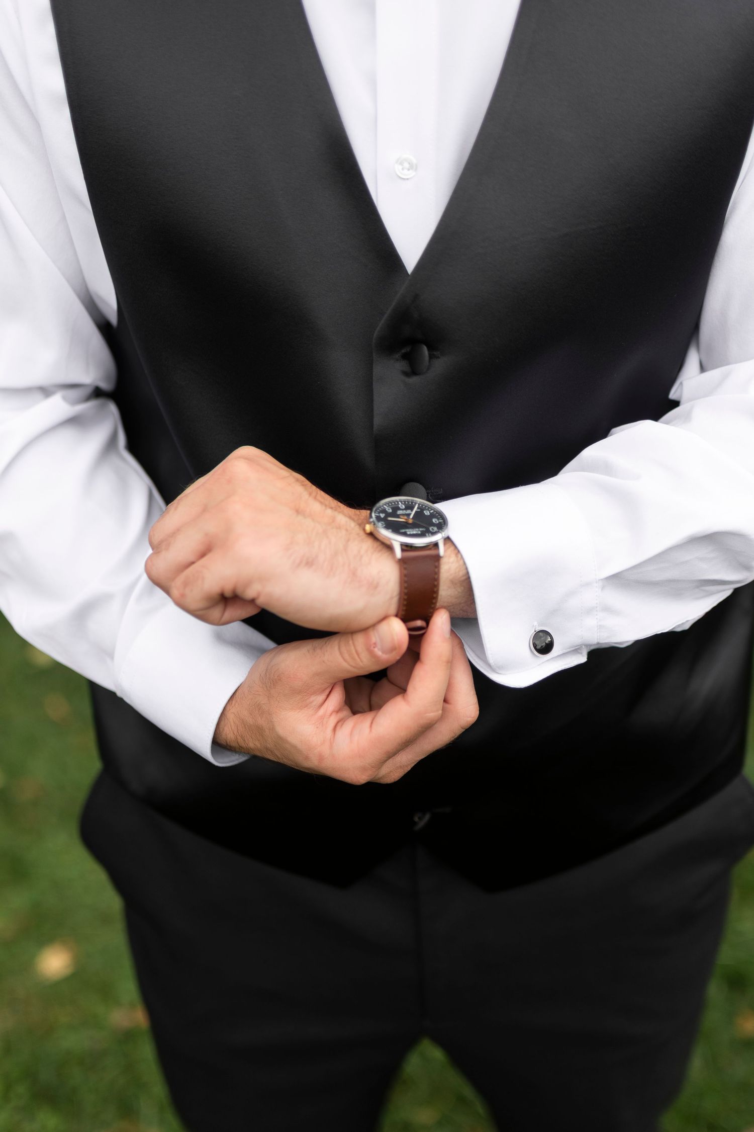 Groom adjusting watch while wearing formal black vest and white shirt.