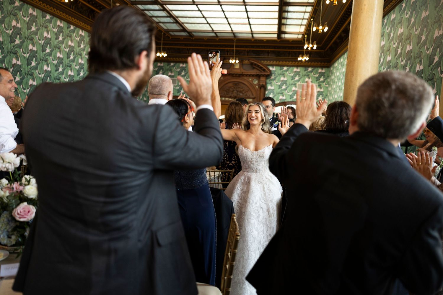 Wedding guests standing and applauding during reception entrance.