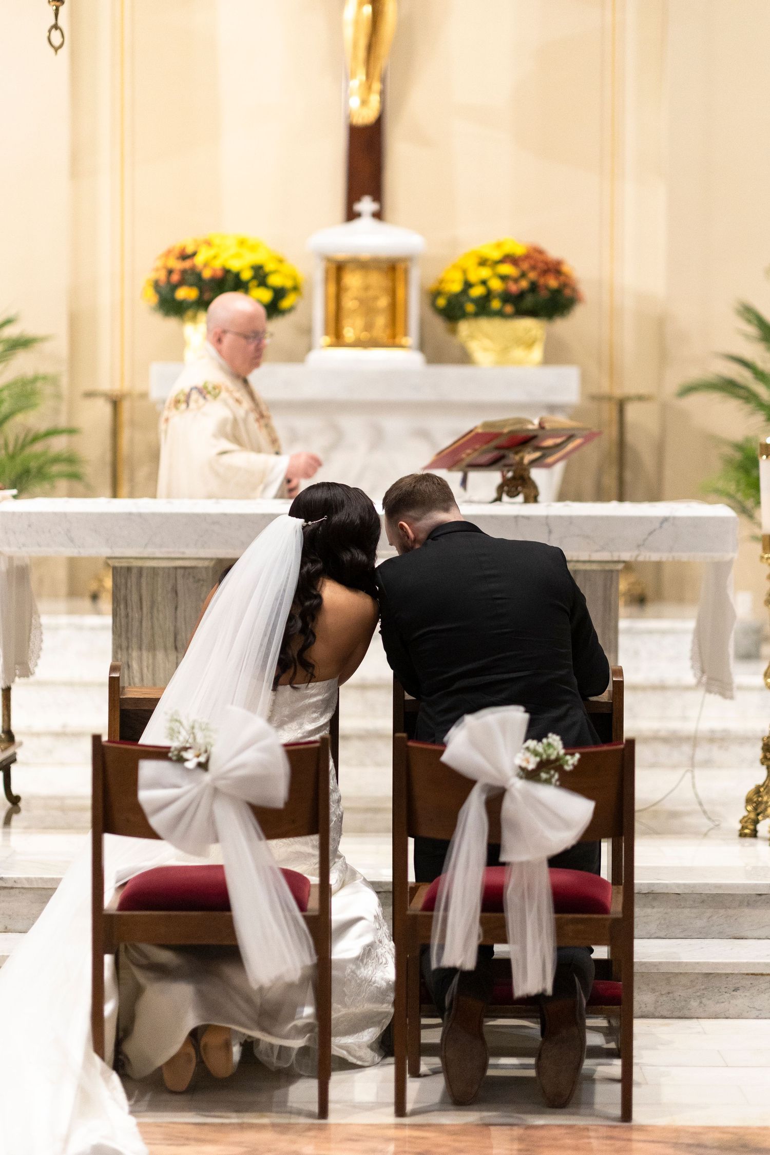 Side view of a couple kneeling at church pews during their wedding ceremony.