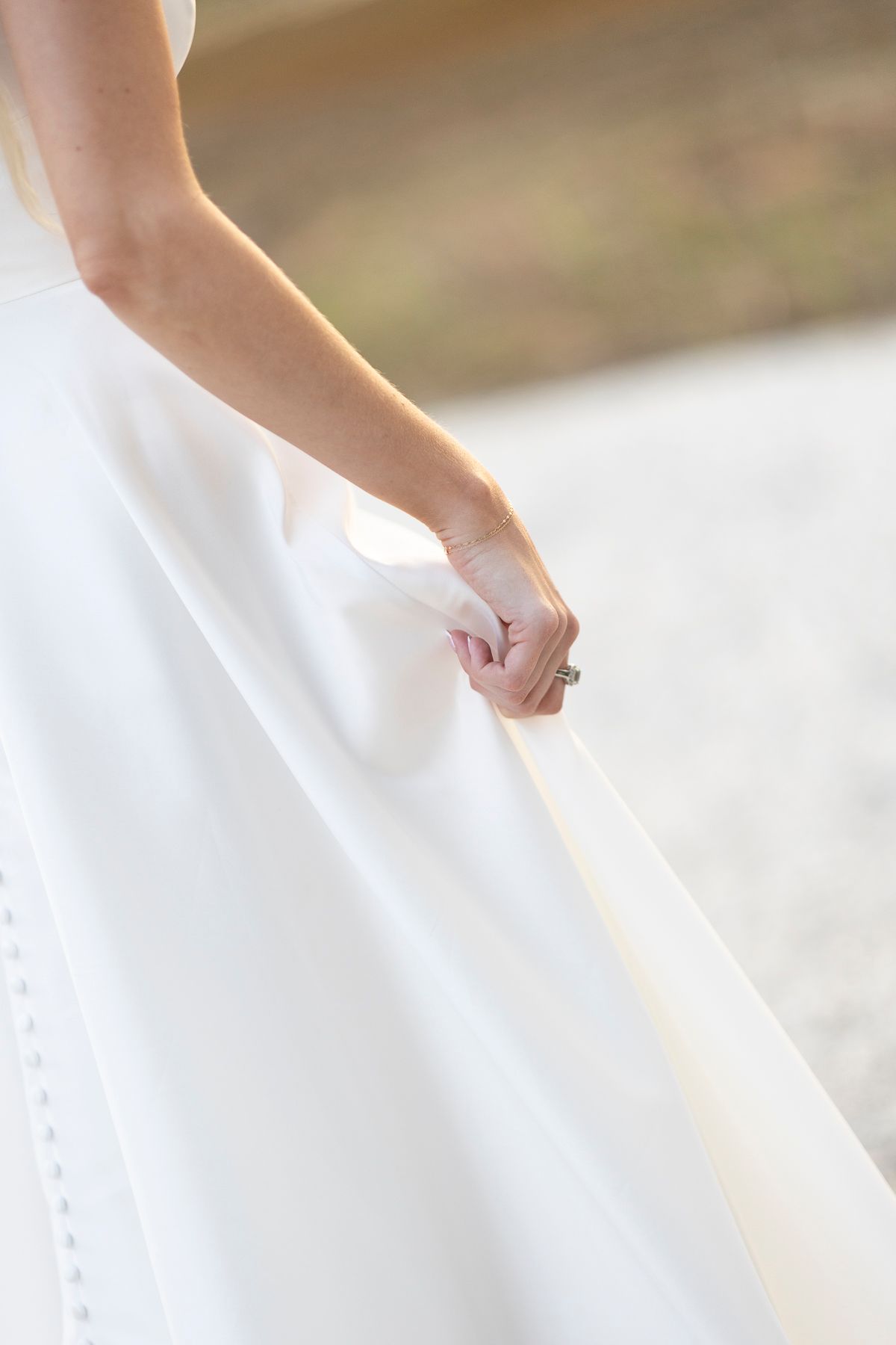 Bride holding her white wedding dress skirt, showcasing an elegant ring on her finger.