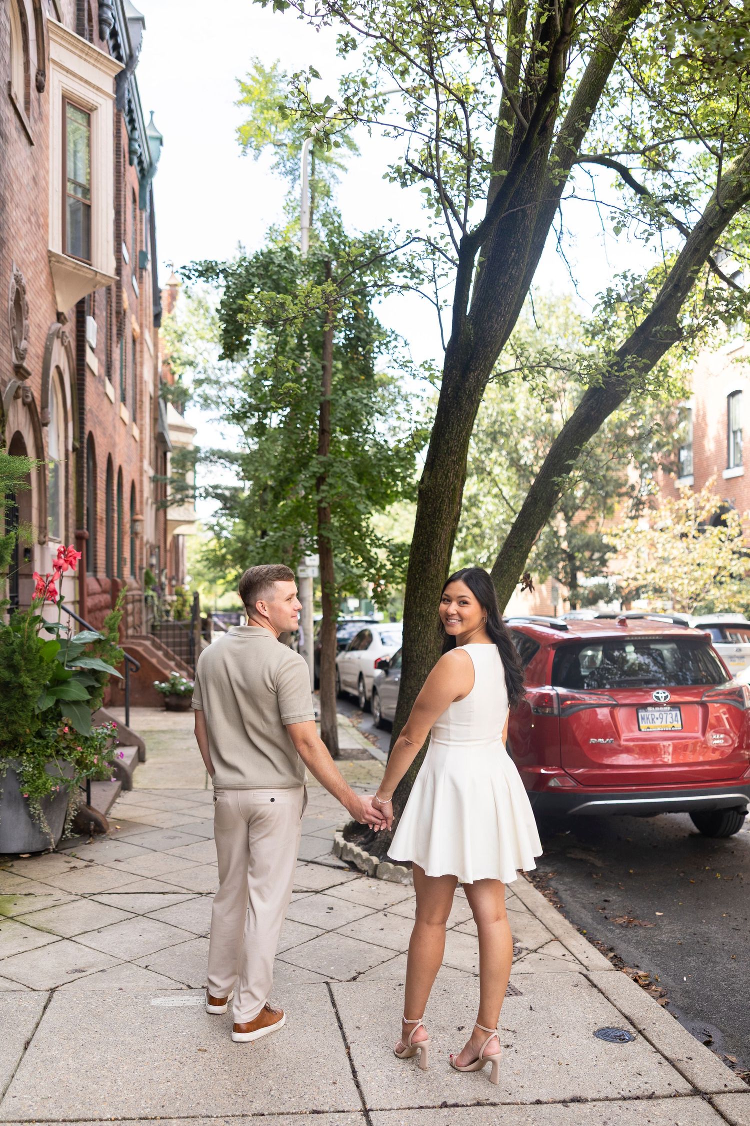 A couple walks hand in hand down a Philadelphia street lined with brownstones.