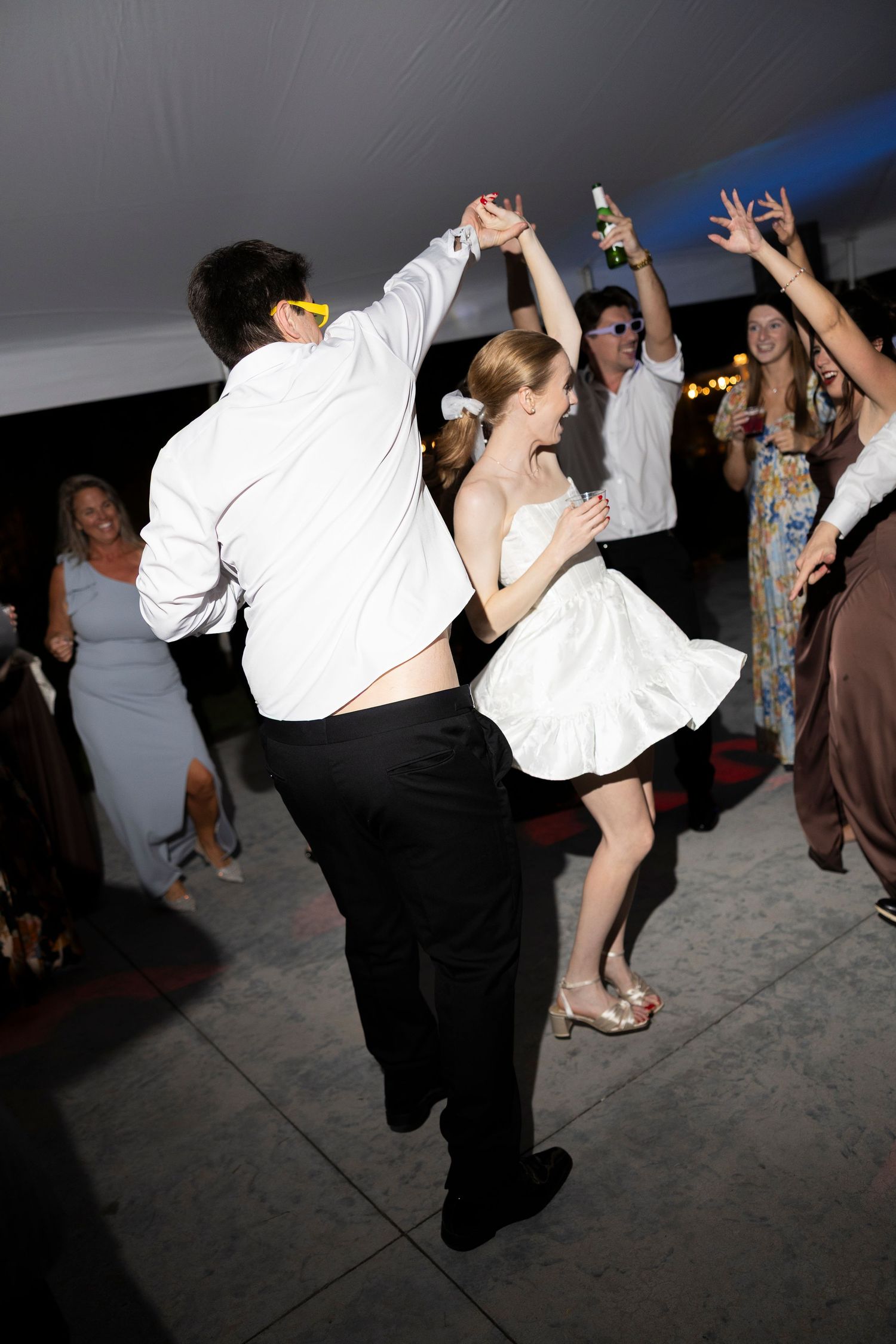 Wedding guests dancing enthusiastically on reception dance floor under tent lighting.