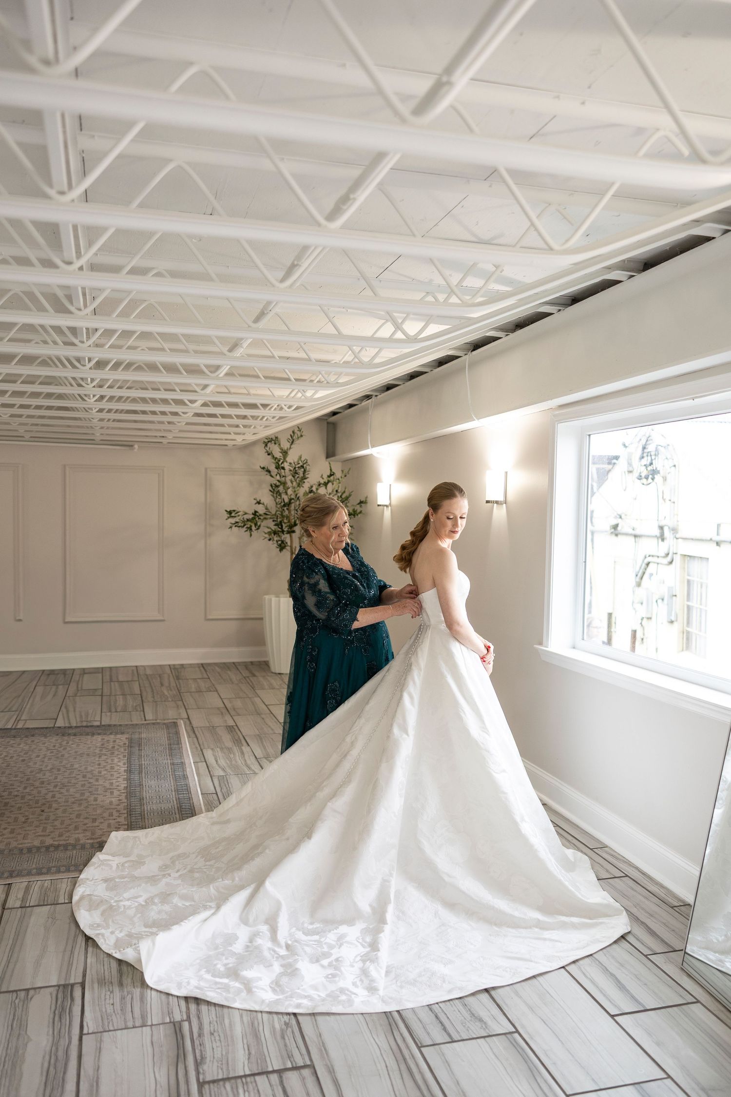 A flowing white wedding gown with train being arranged in a bright studio space.