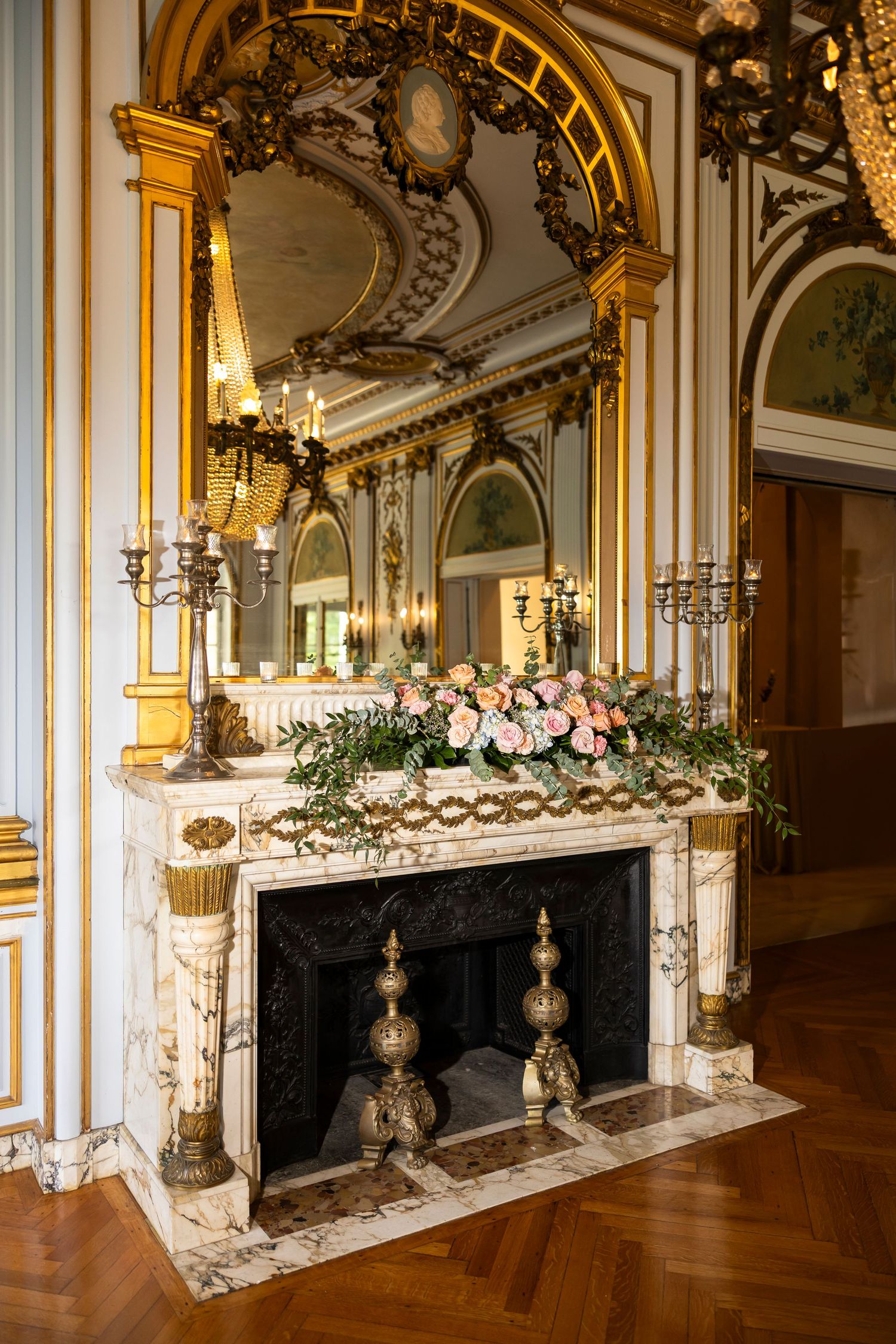 Ornate ballroom with gilded mirrors and floral arrangements decorating the mantels.