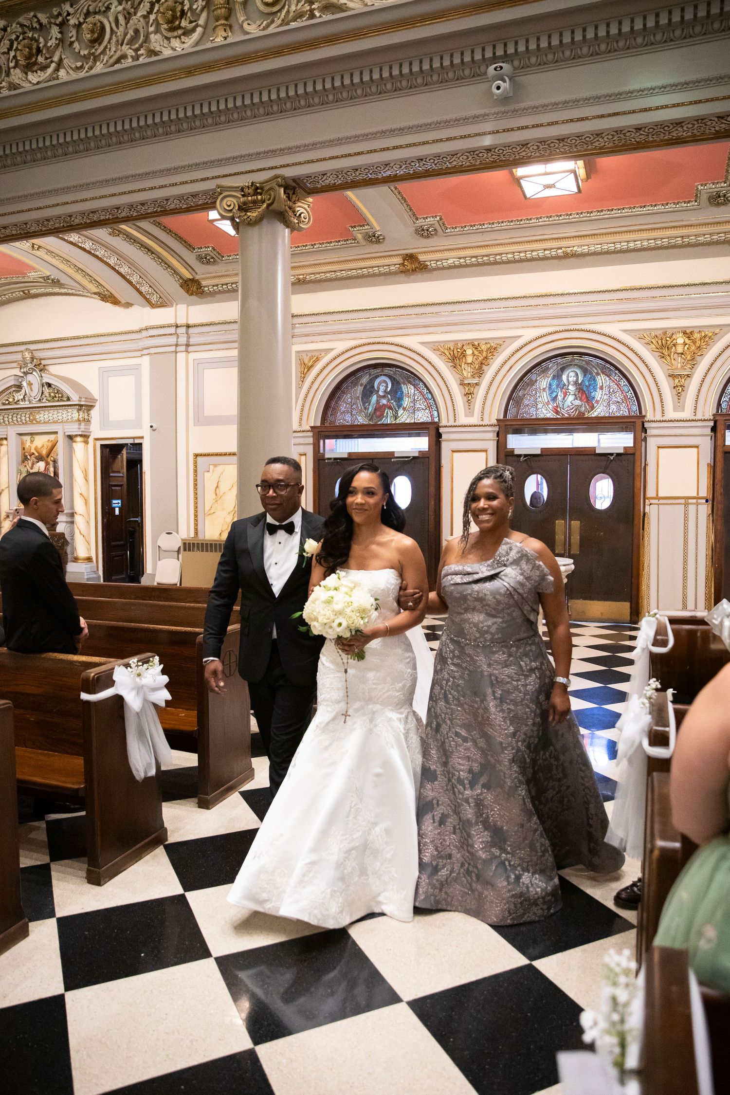 Wedding party gathered in an ornate church with classical architecture and checkered flooring.