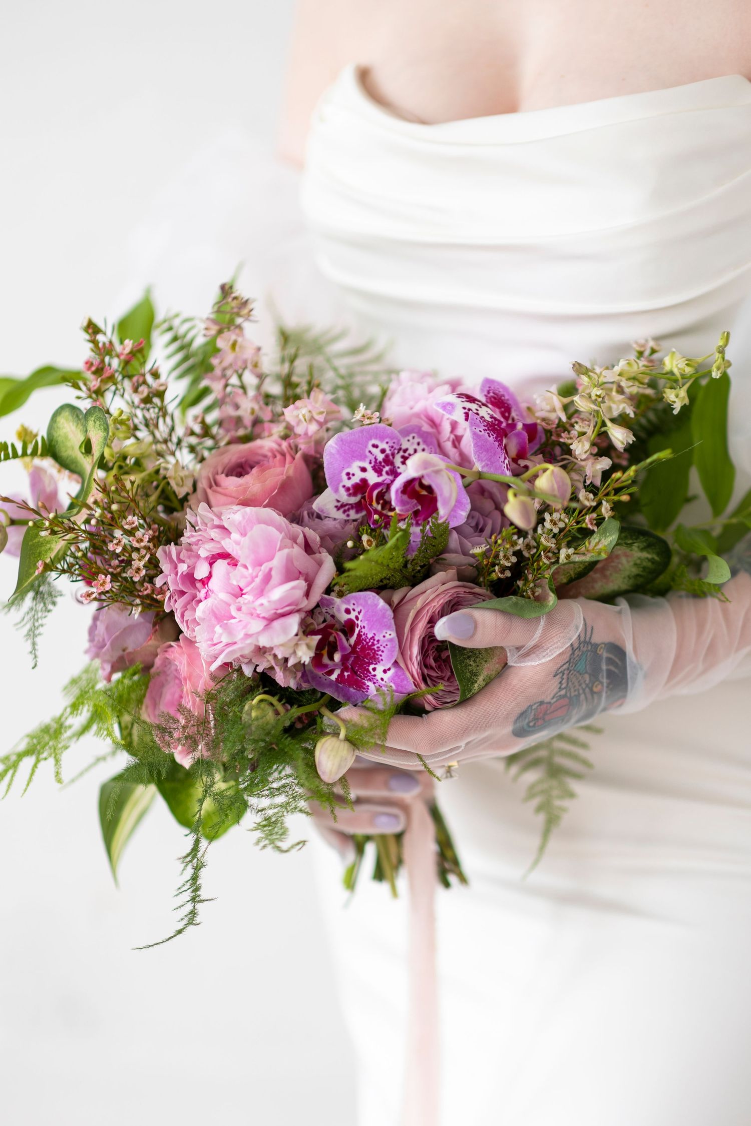 Beautiful floral arrangement featuring pink peonies, orchids and greenery against a white background.
