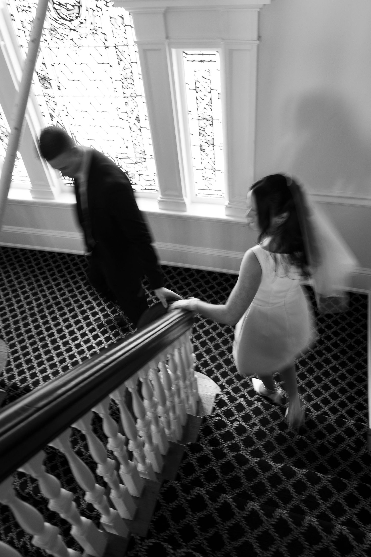 A black and white photo of a couple descending an elegant staircase with patterned carpet.