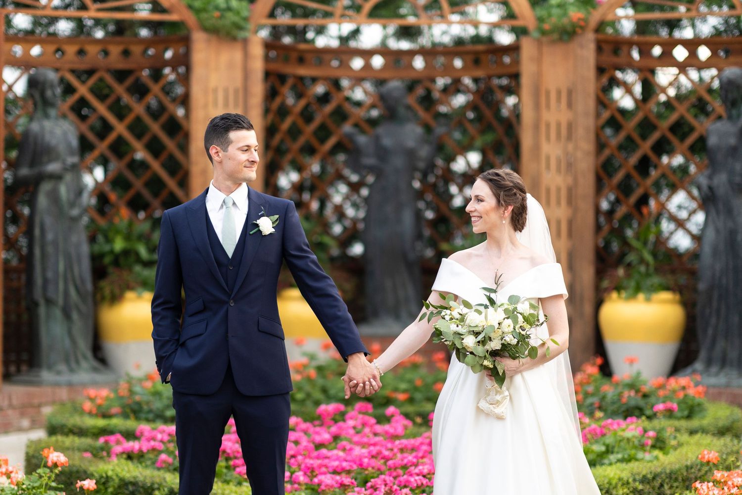Couple poses for portraits in a garden setting with vibrant pink flowers and wooden lattice backdrop.