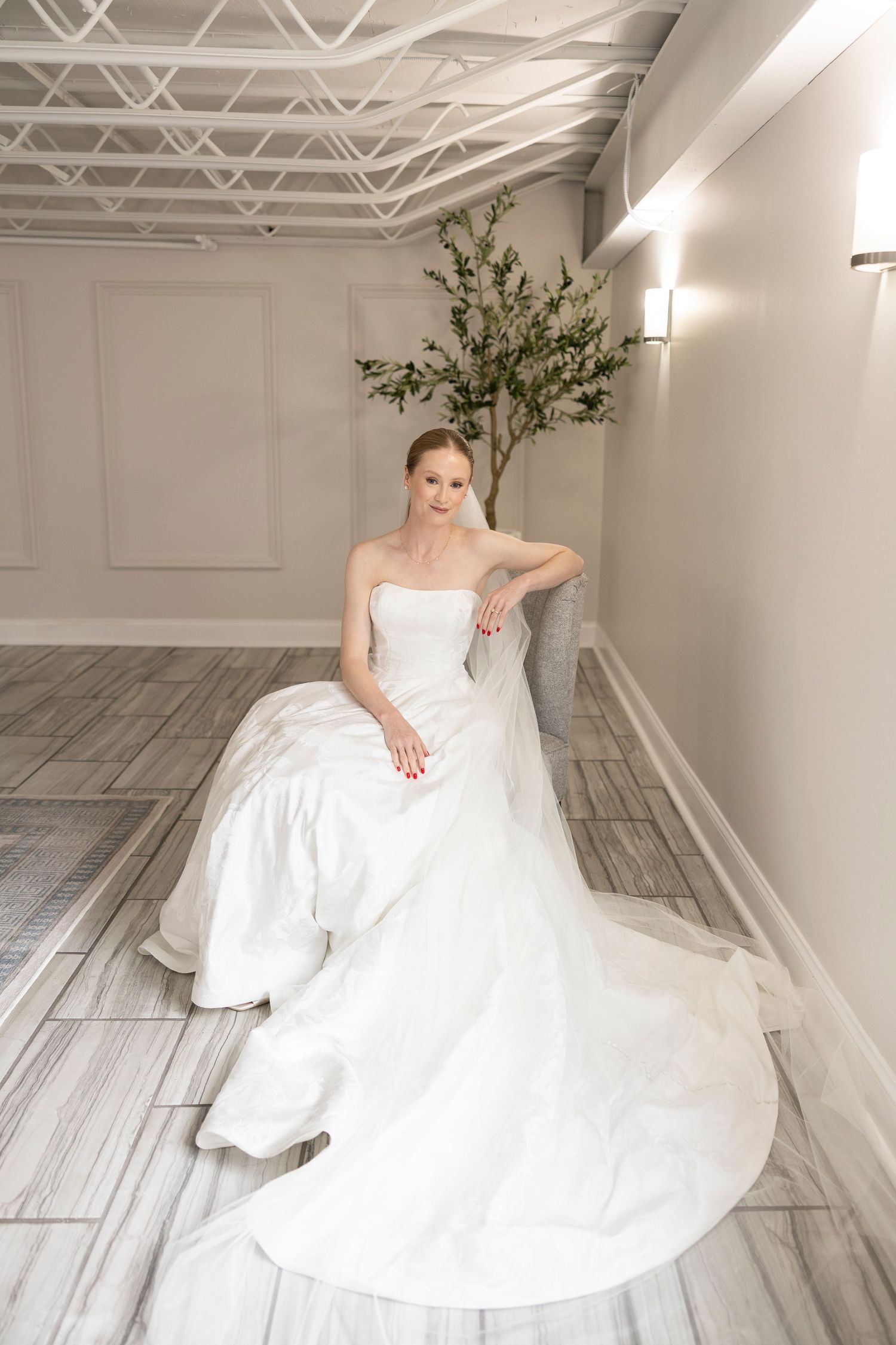 Bride in a strapless white ball gown with a long train, seated gracefully on a marble floor in an elegant room.