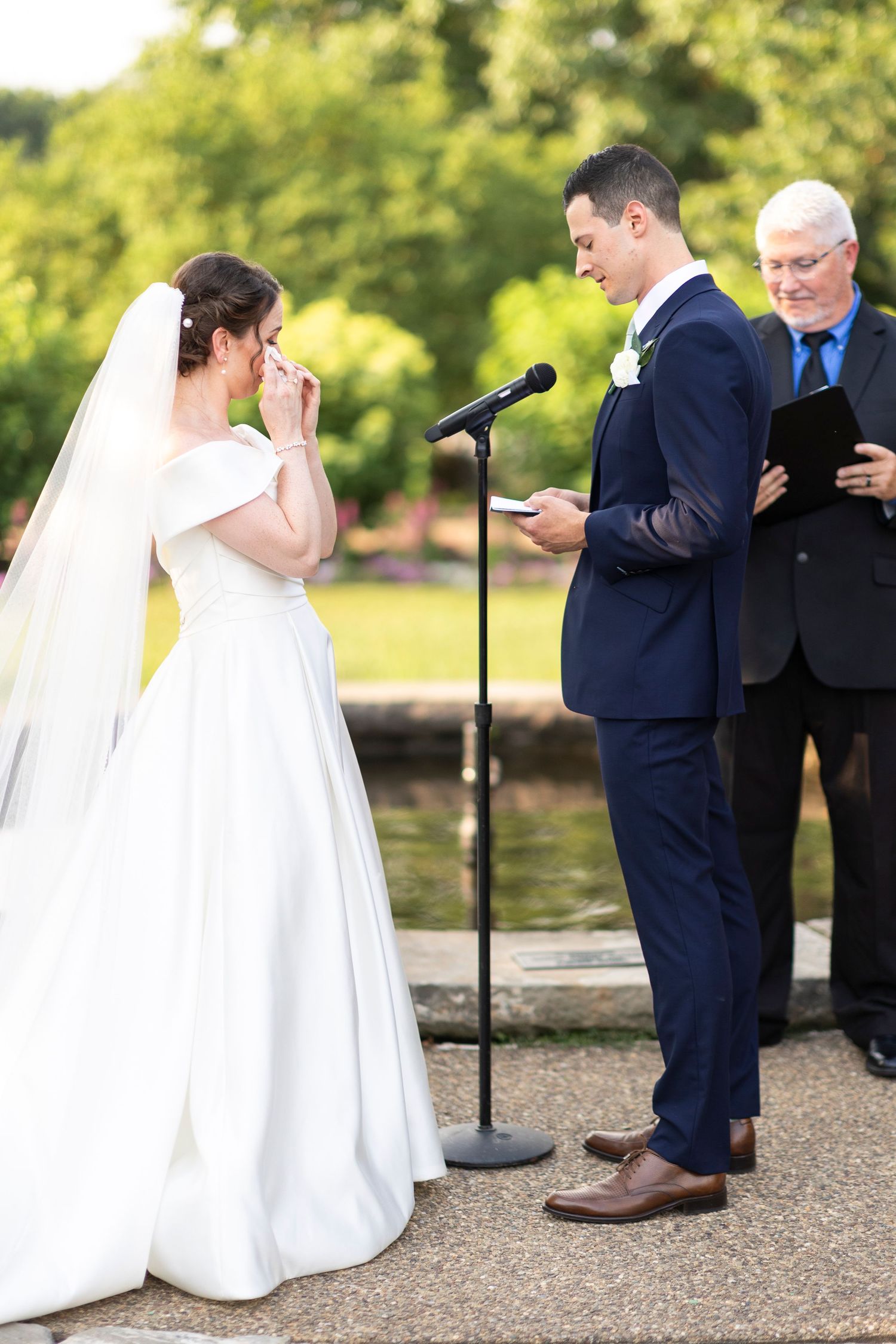 Emotional wedding ceremony moment as couple reads vows at outdoor garden venue.