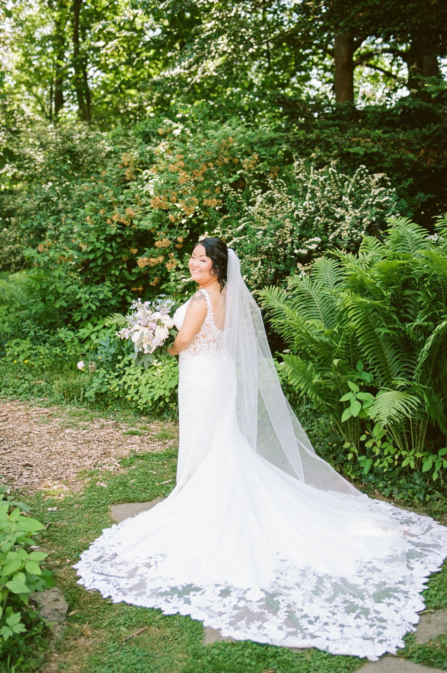 Elegant wedding dress with long lace train photographed in a garden setting.