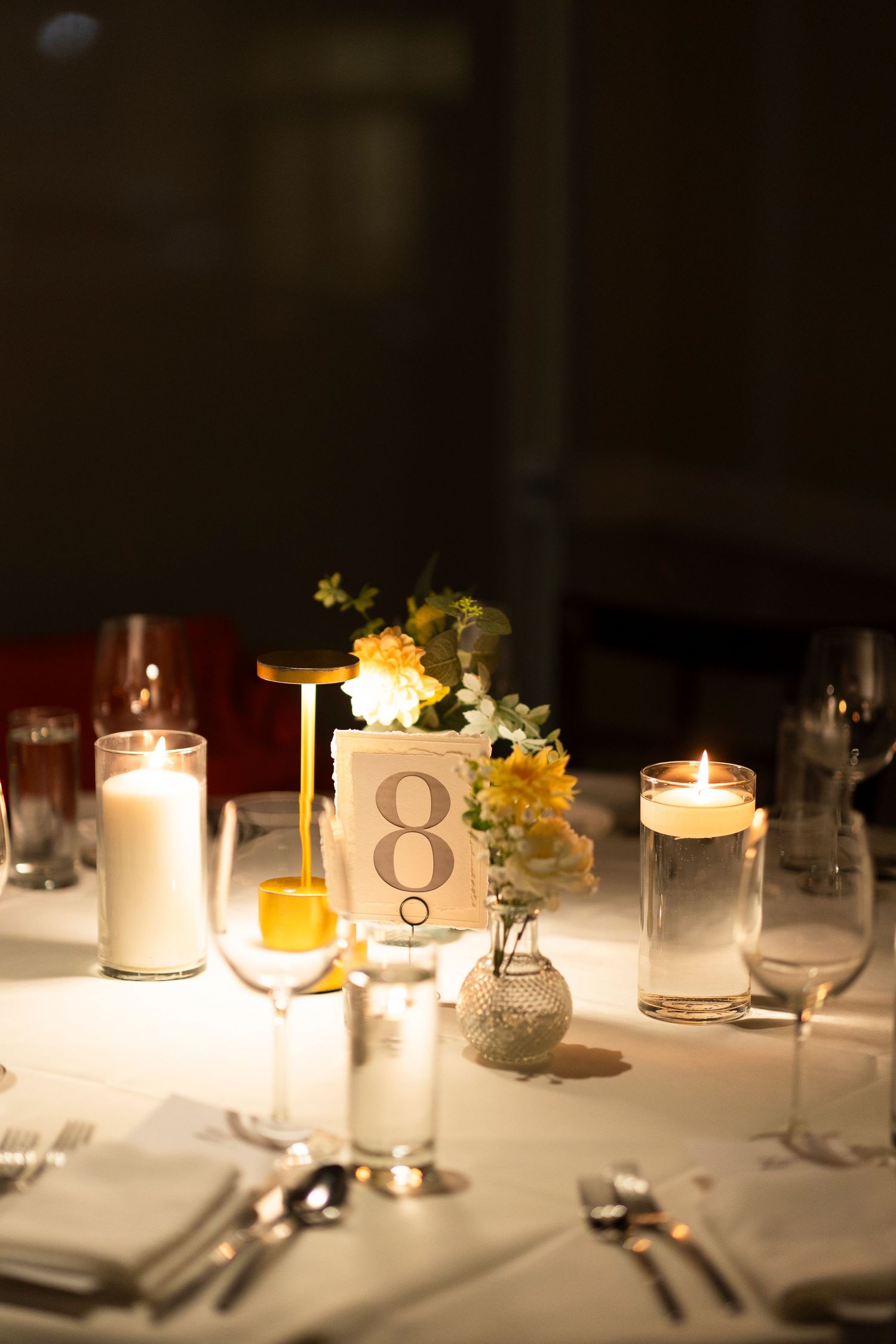 Wedding reception table decorated with candles and table numbers in soft lighting.