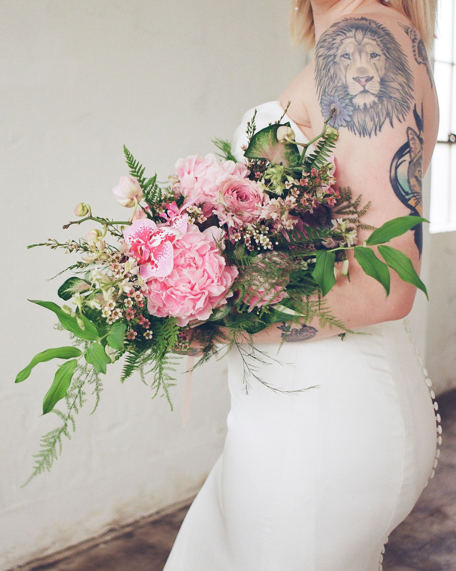 Close-up details of pink peony bridal bouquet with greenery against white background.