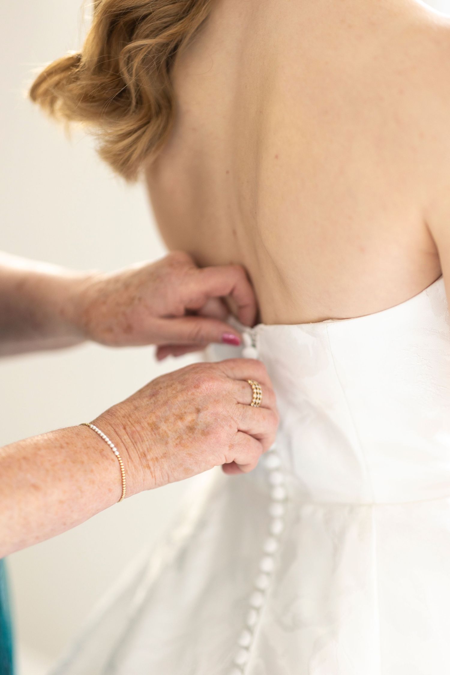 Close-up shots of buttons being fastened on the back of a white wedding dress.