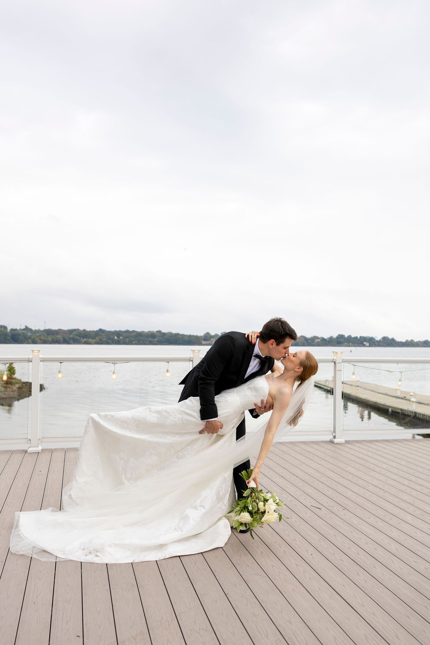 A romantic dip pose during a waterfront wedding photoshoot on a wooden deck.