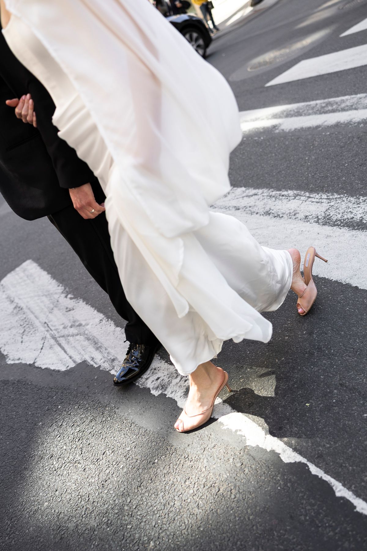 Bride in white gown and heels crossing a zebra crossing with groom in black suit on their wedding day.