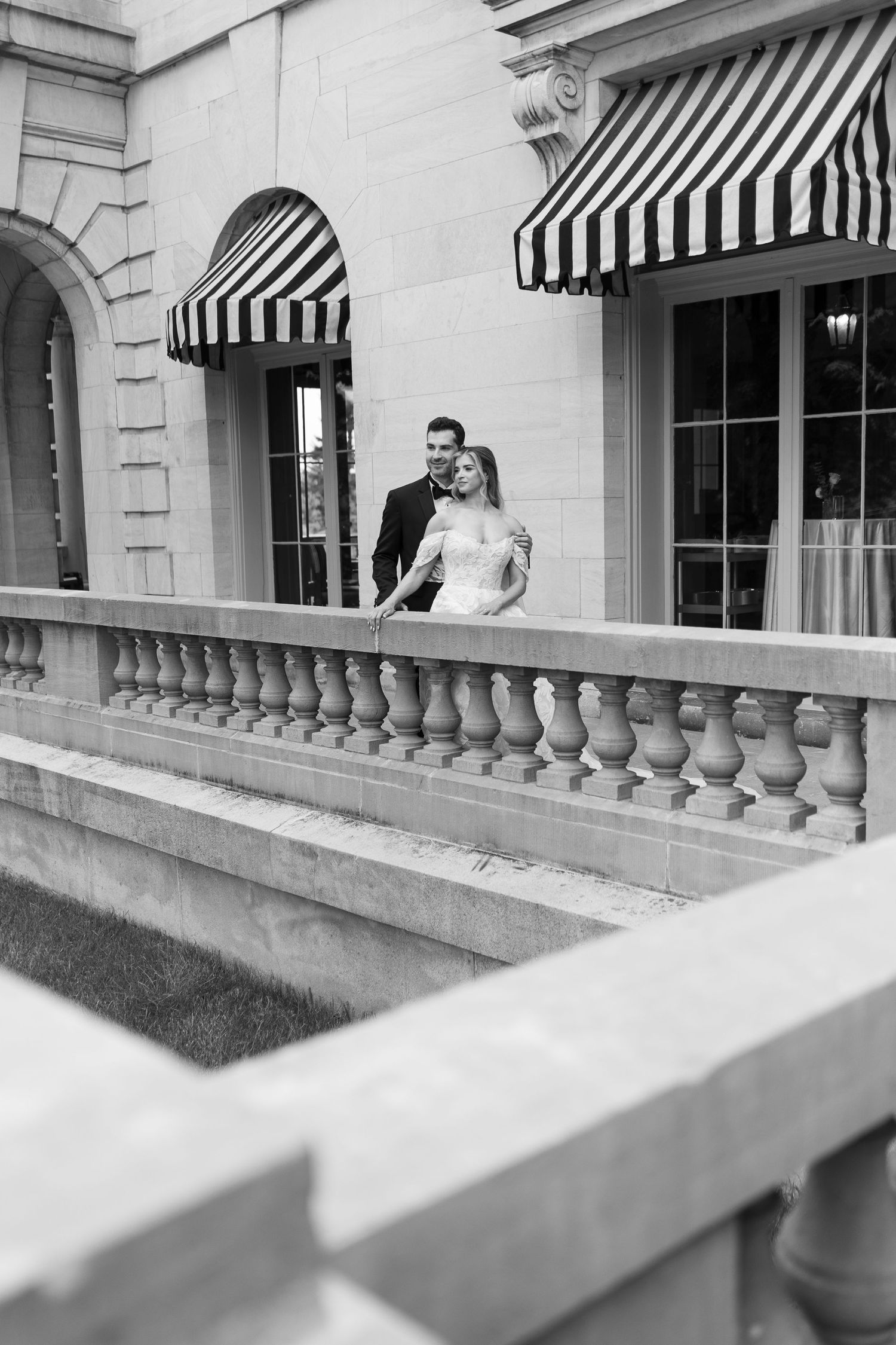 Black and white wedding photo showing couple on balcony with striped awnings.
