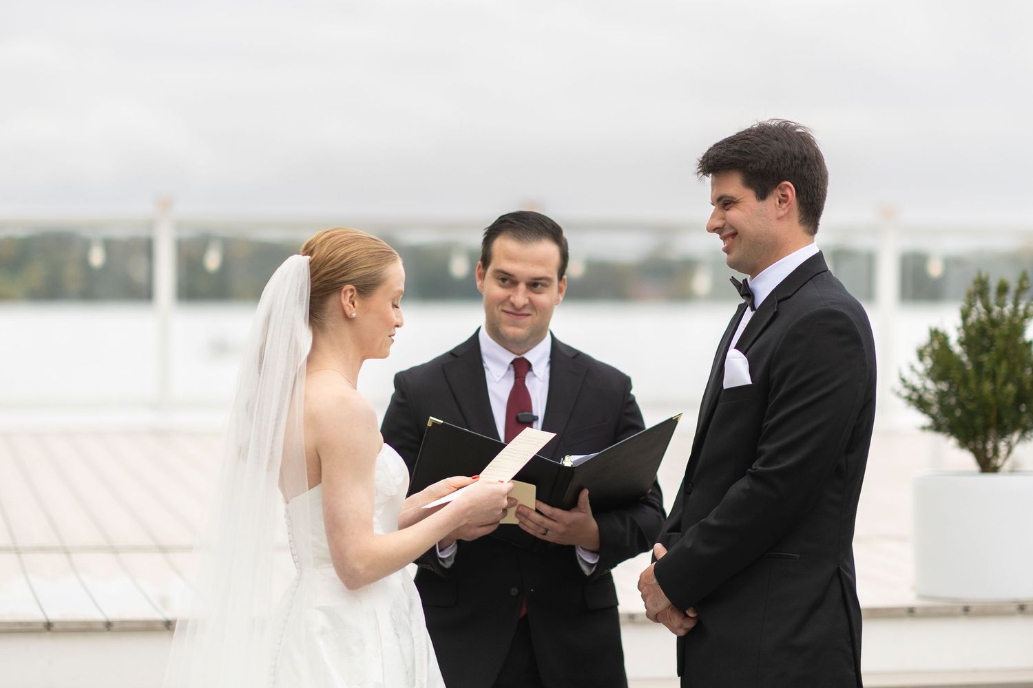 Intimate outdoor wedding ceremony with attendees gathered on a waterfront deck.