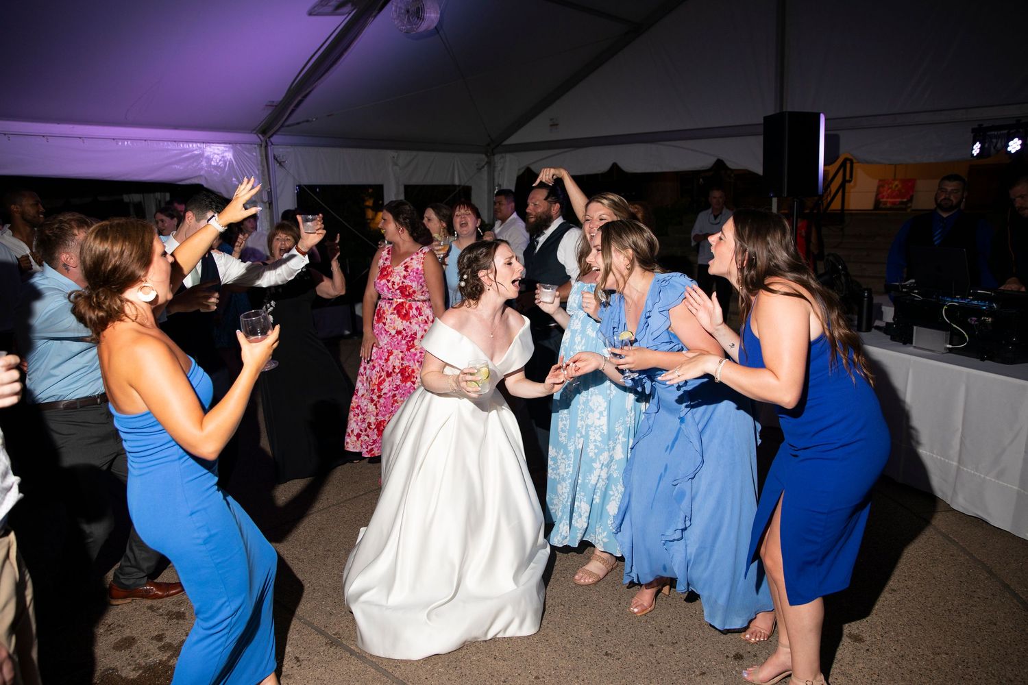 Wedding reception dance floor filled with guests under purple ambient lighting.