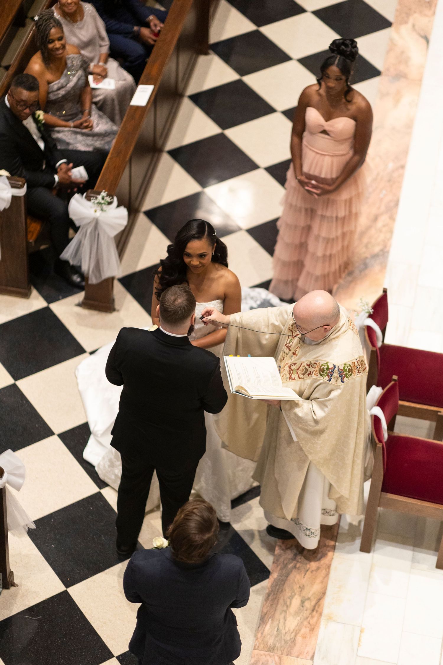 A couple shares an intimate moment during their wedding ceremony in a church with a black and white checkered floor.