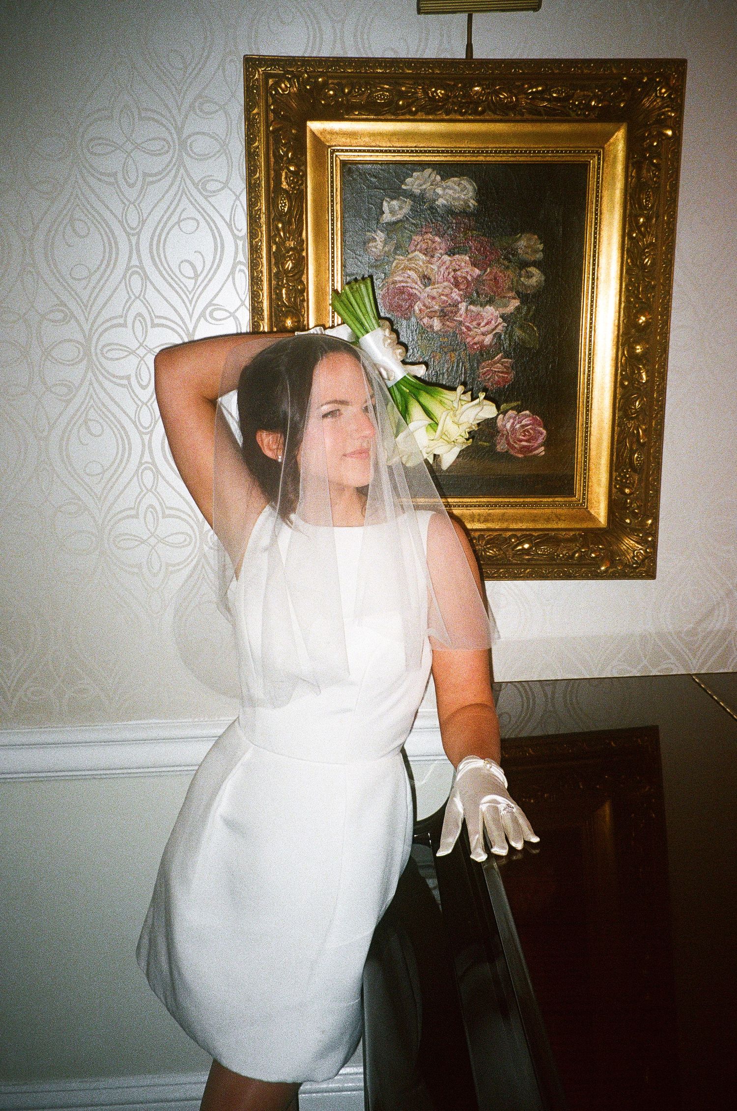 Bride posing dramatically against wallpapered room with vintage artwork.